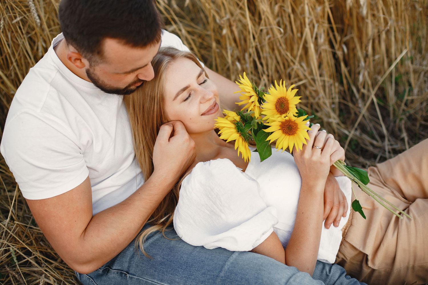 Romantic couple embraces in golden field with bright sunflowers during intimate outdoor photoshoot.