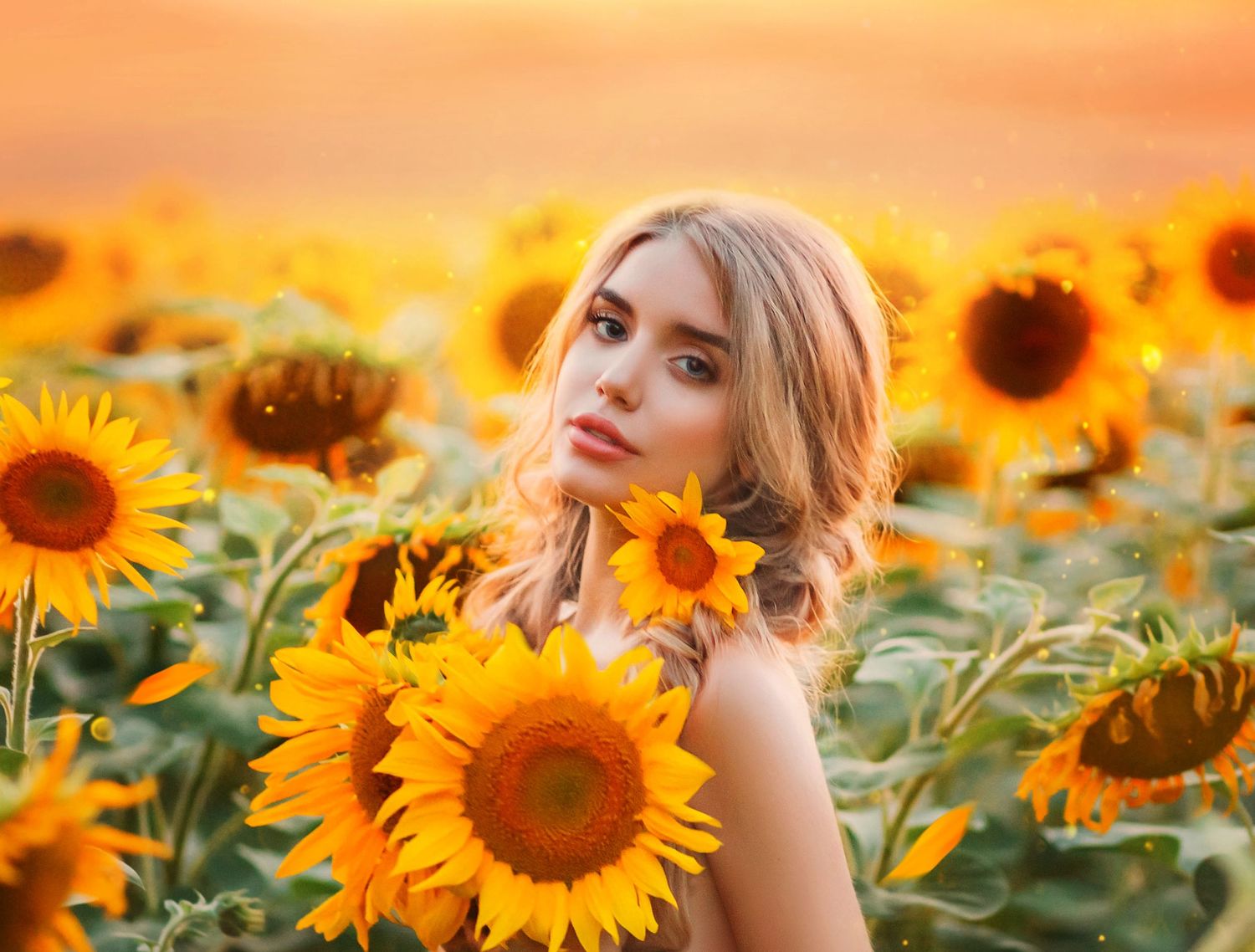 A person poses thoughtfully in a vibrant field of blooming sunflowers during golden sunset light.