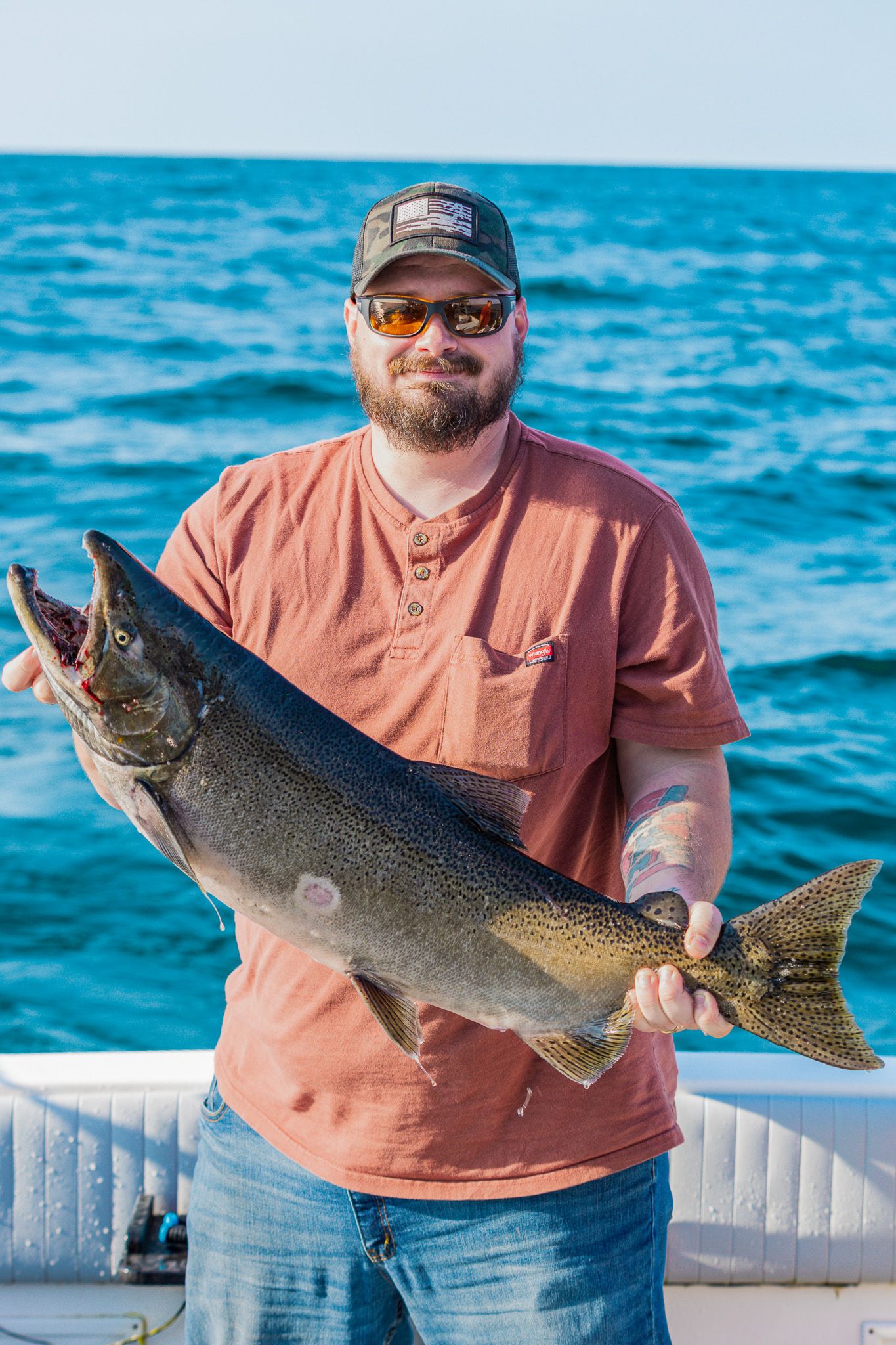 A series of photos showing a lake trout being displayed on a boat with bright blue water in the background.
