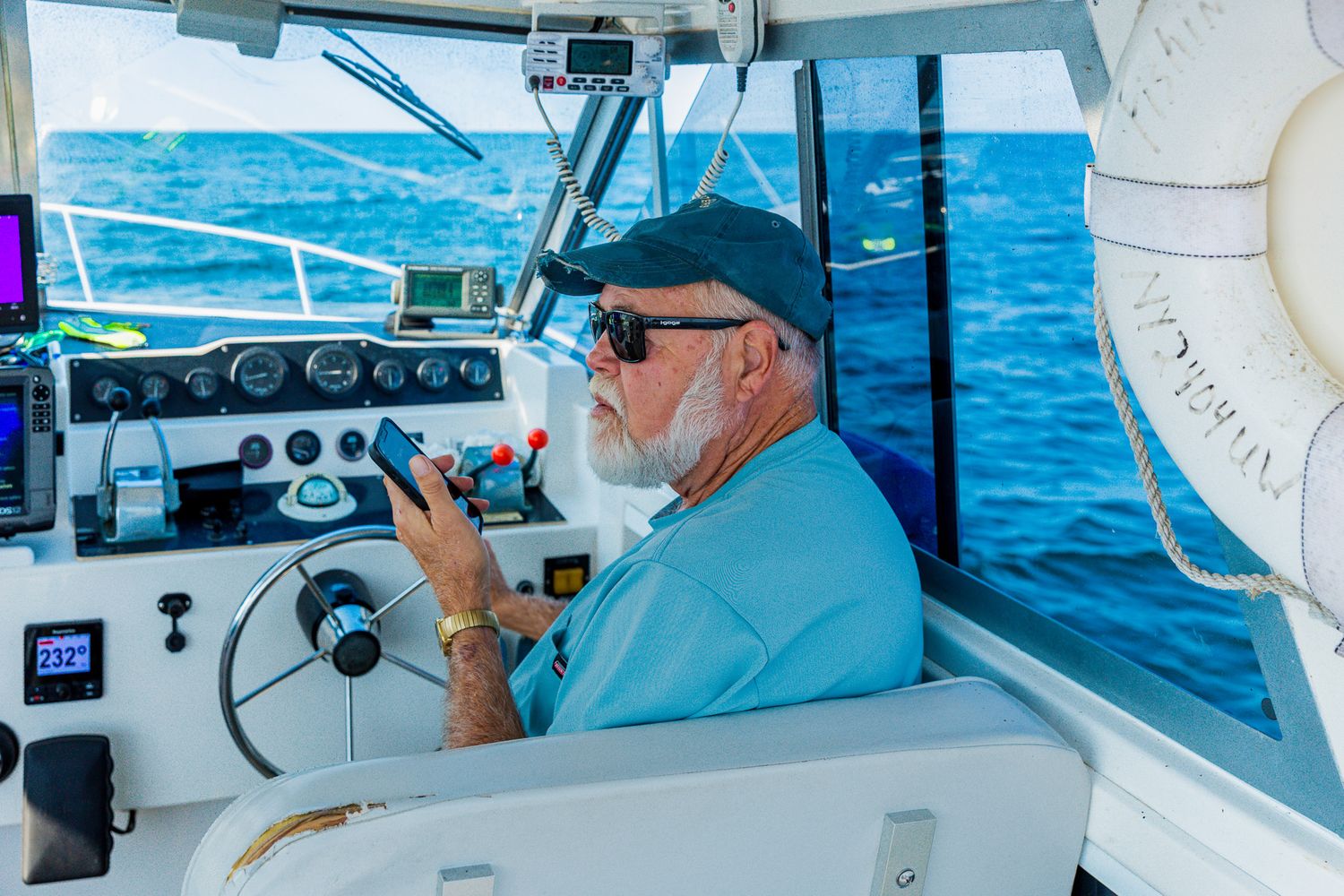 Captain at helm of sport fishing boat navigates through blue waters while using marine electronics and controls.