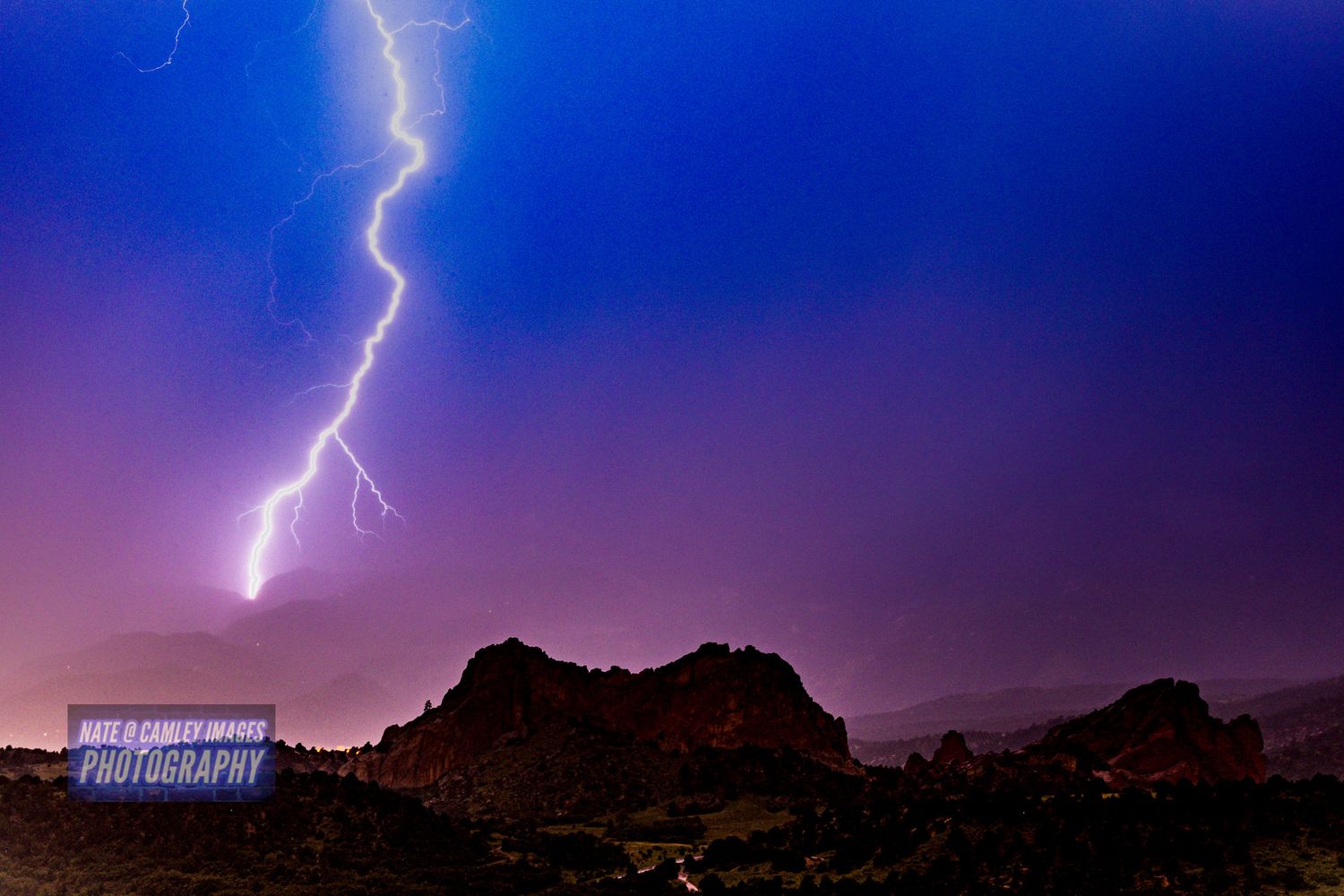 Lightning bolts illuminate the night sky over a mountainous landscape during a dramatic thunderstorm.