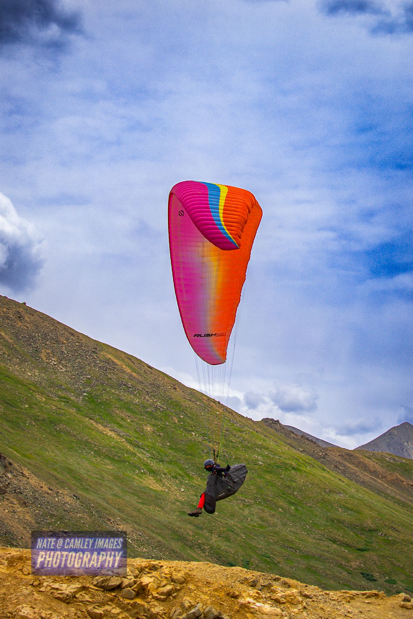 A paraglider with a vibrant red and pink wing soars against blue skies and green mountain slopes in sequence.