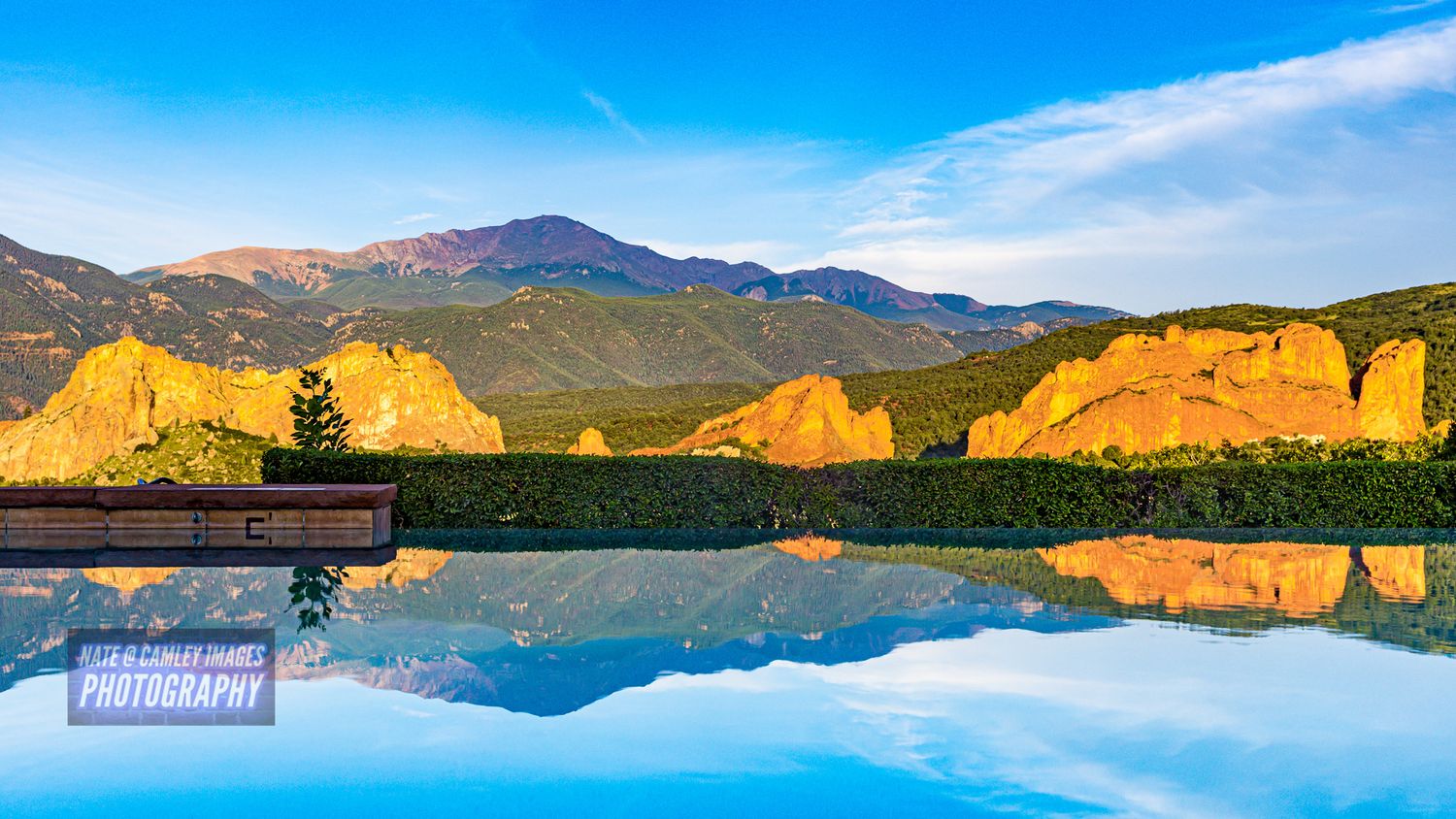 Panoramic view of a tranquil mountain lake reflecting golden cliffs and blue sky during sunset.
