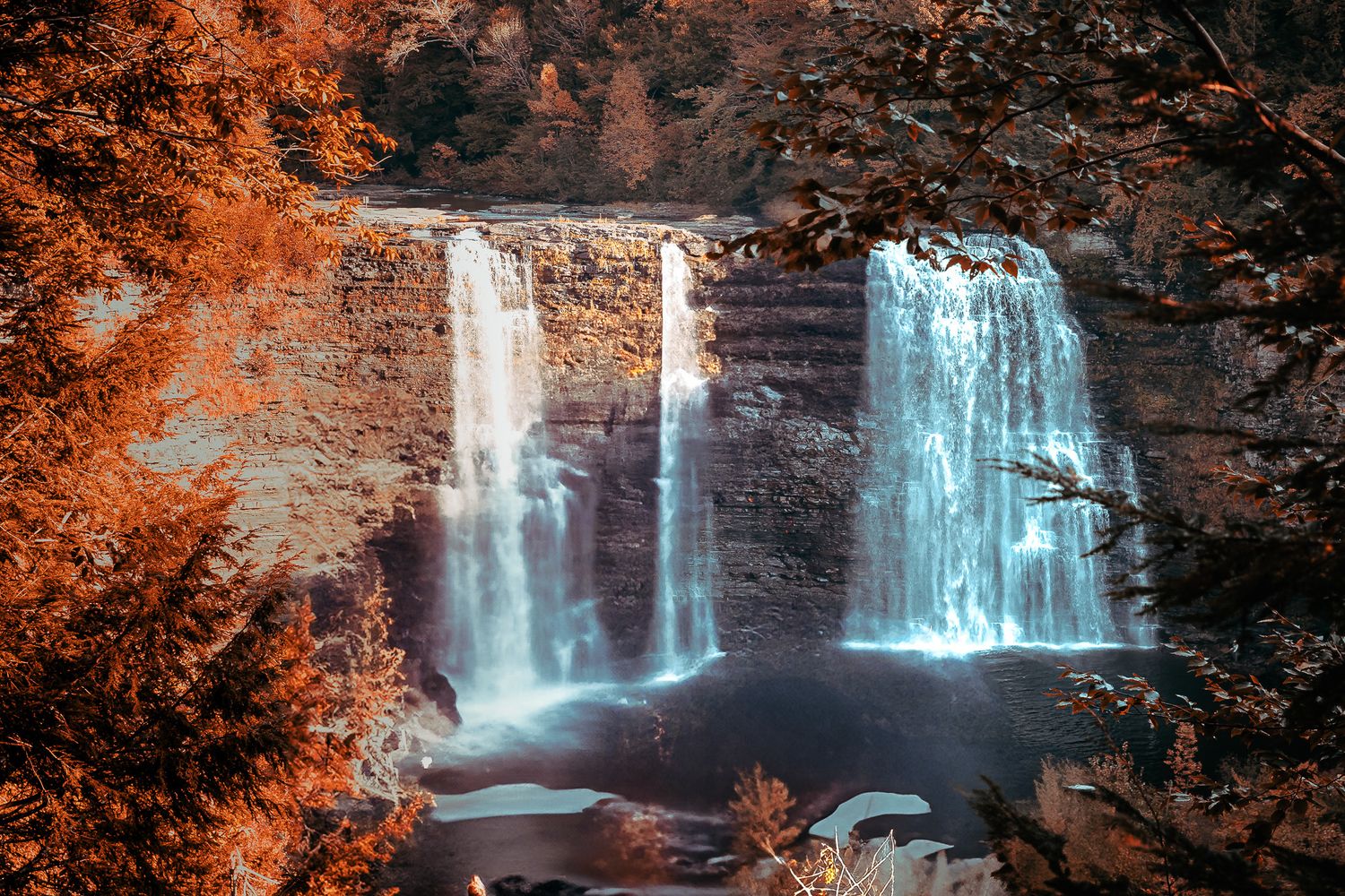 Majestic waterfall cascades down rocky cliffs surrounded by autumn foliage with ethereal blue and orange color contrast.