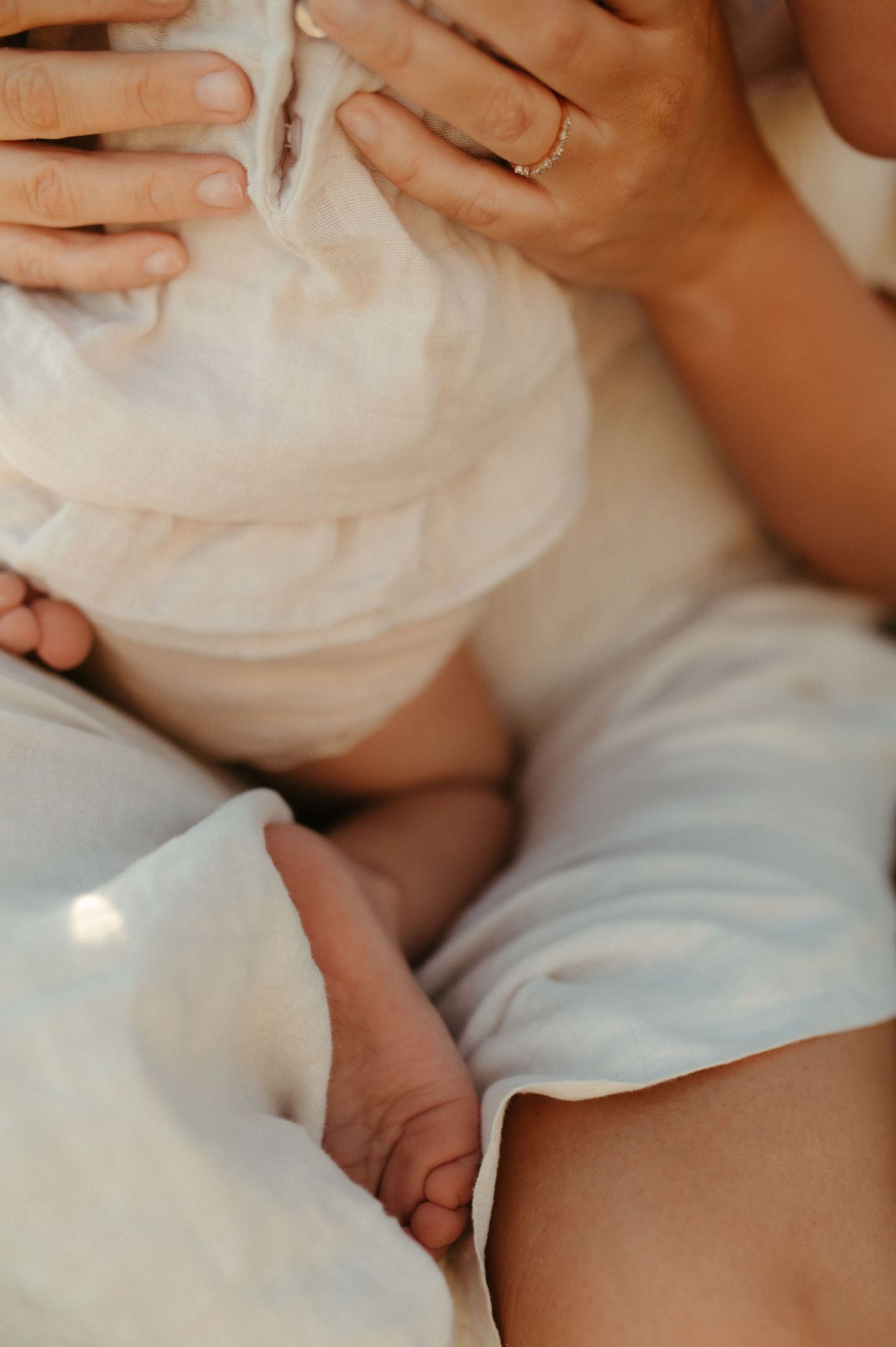 A mother tenderly holds her newborn baby wrapped in a soft white muslin cloth, with tiny feet peeking out.