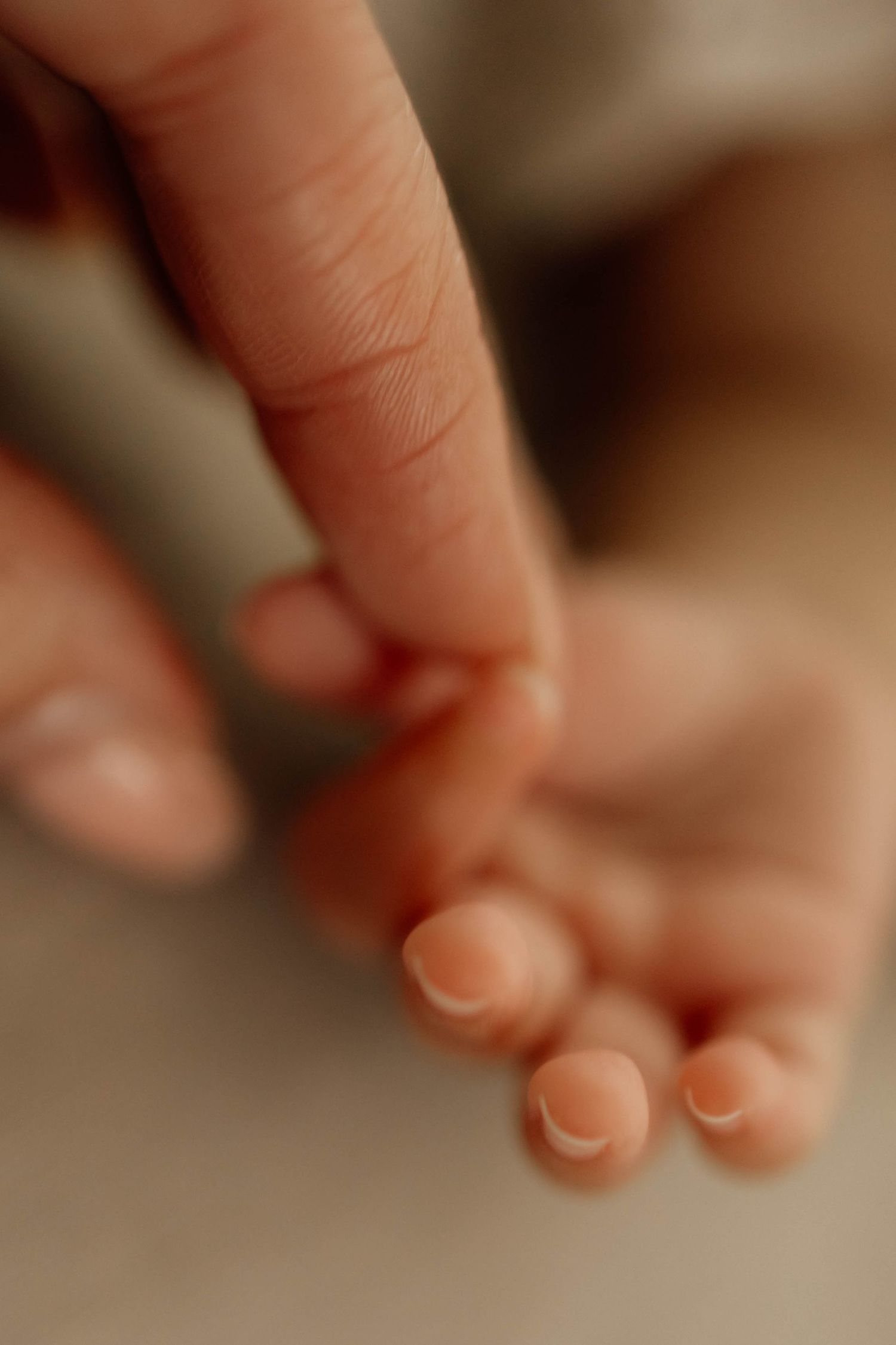 Close-up of an adult finger gently touching tiny newborn baby toes, capturing a tender moment of new parenthood.