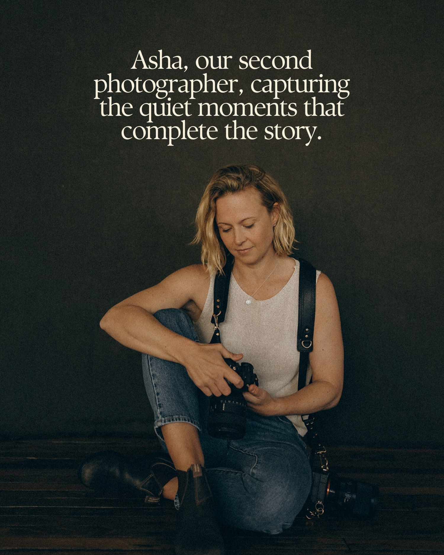 Photographer Asha kneeling and adjusting her camera, wearing a white tank top and jeans against a dark background.