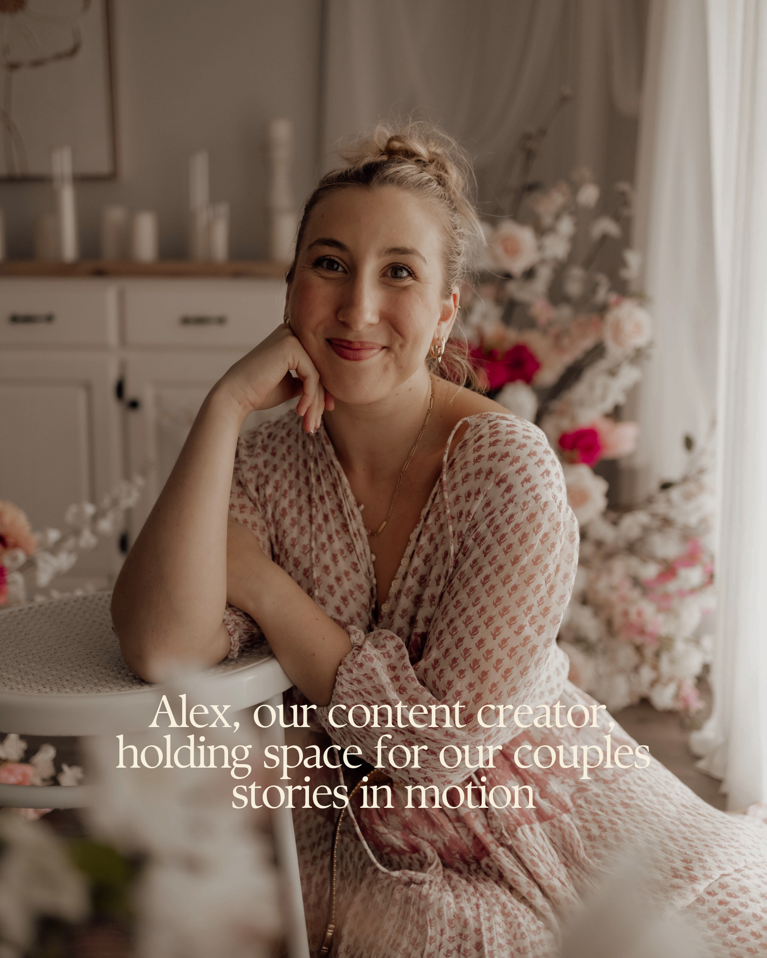 Alex, a smiling content creator in a floral dress, poses gracefully in a romantic floral studio setting.