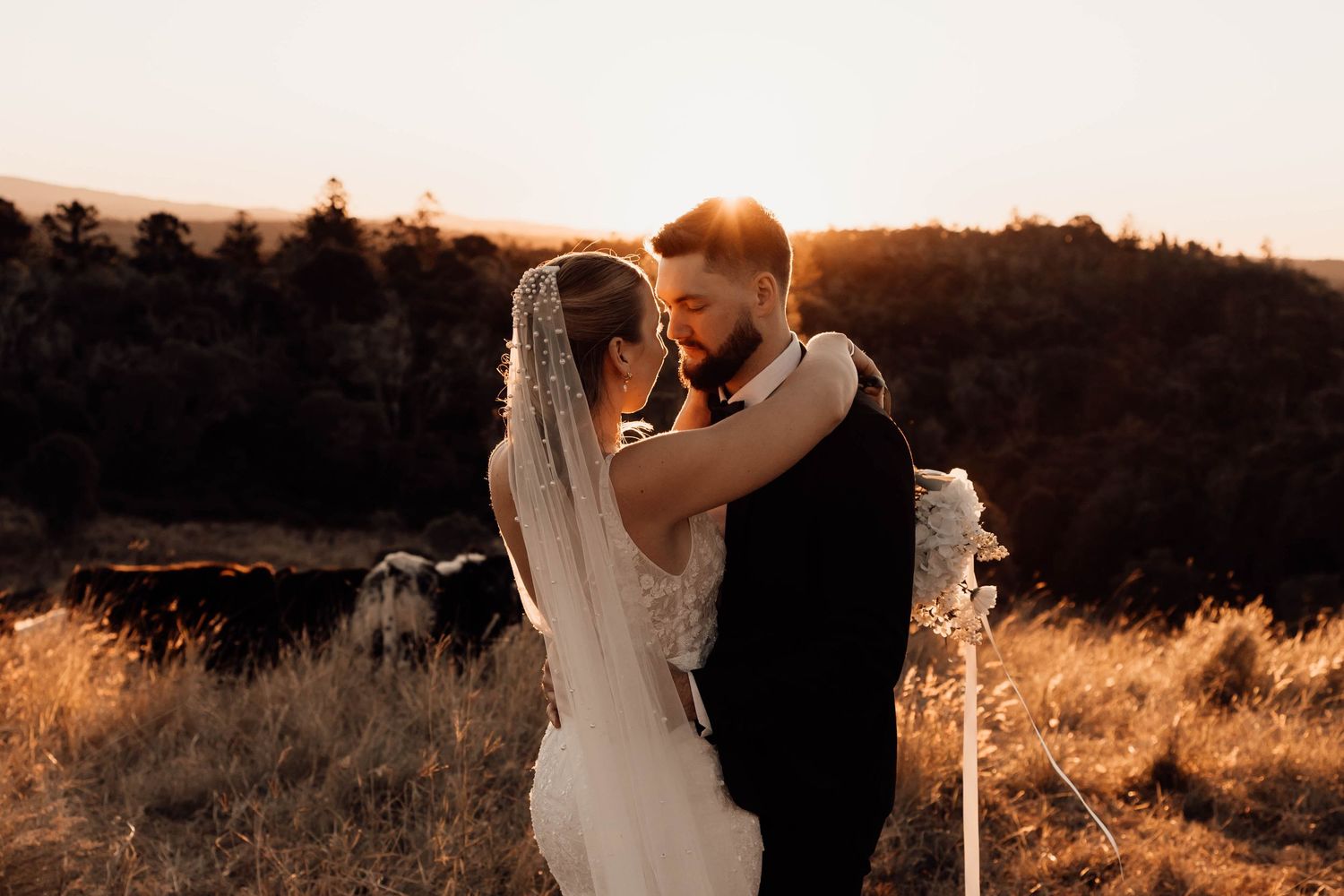 A bride and groom share a romantic moment at golden hour in a scenic outdoor setting during their wedding ceremony.