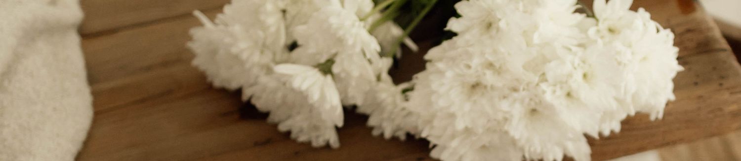 White carnations arranged on a wooden surface, showcasing fresh blooms with delicate petals.