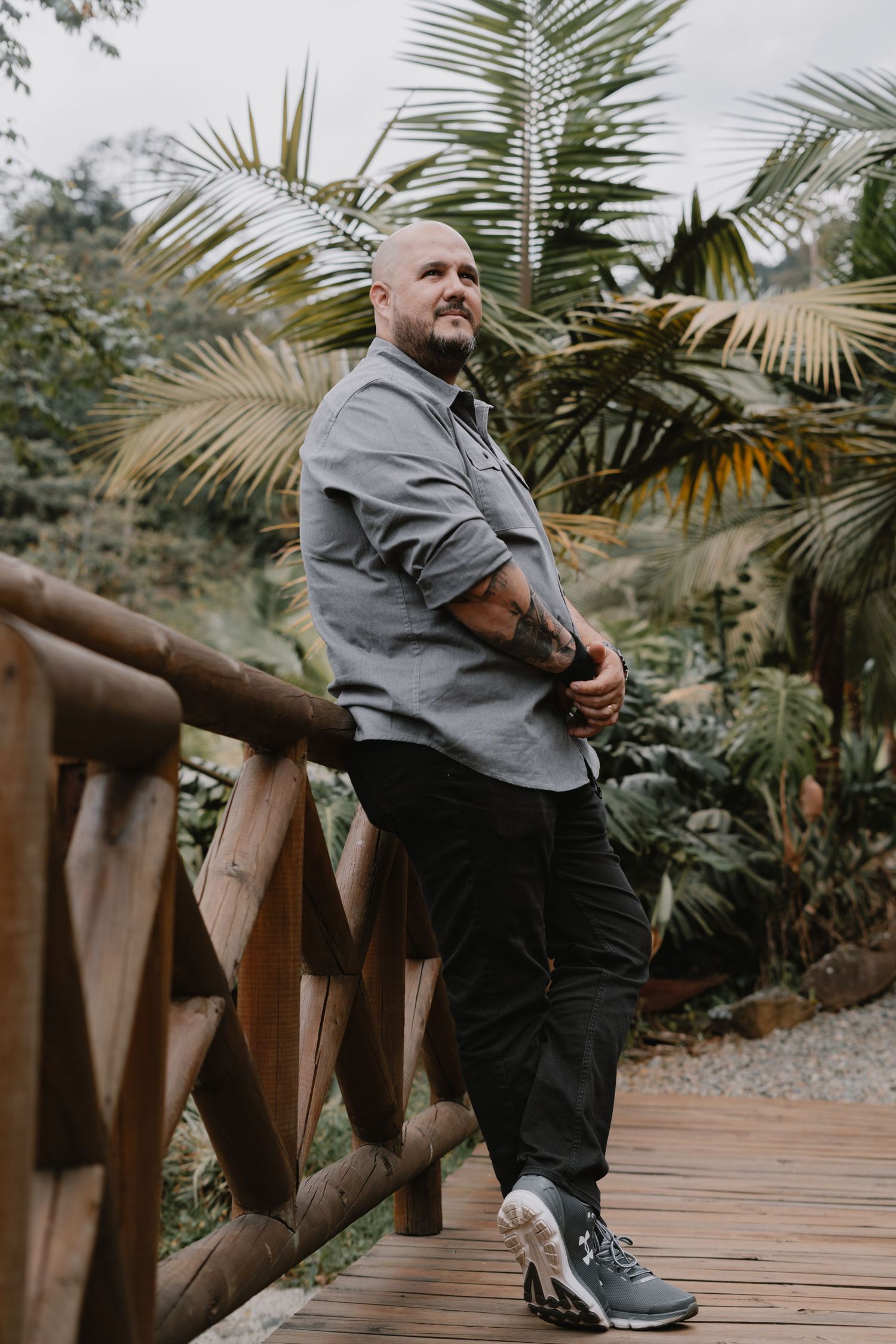 A person in a grey shirt sits on a wooden walkway surrounded by palm trees and tropical foliage.