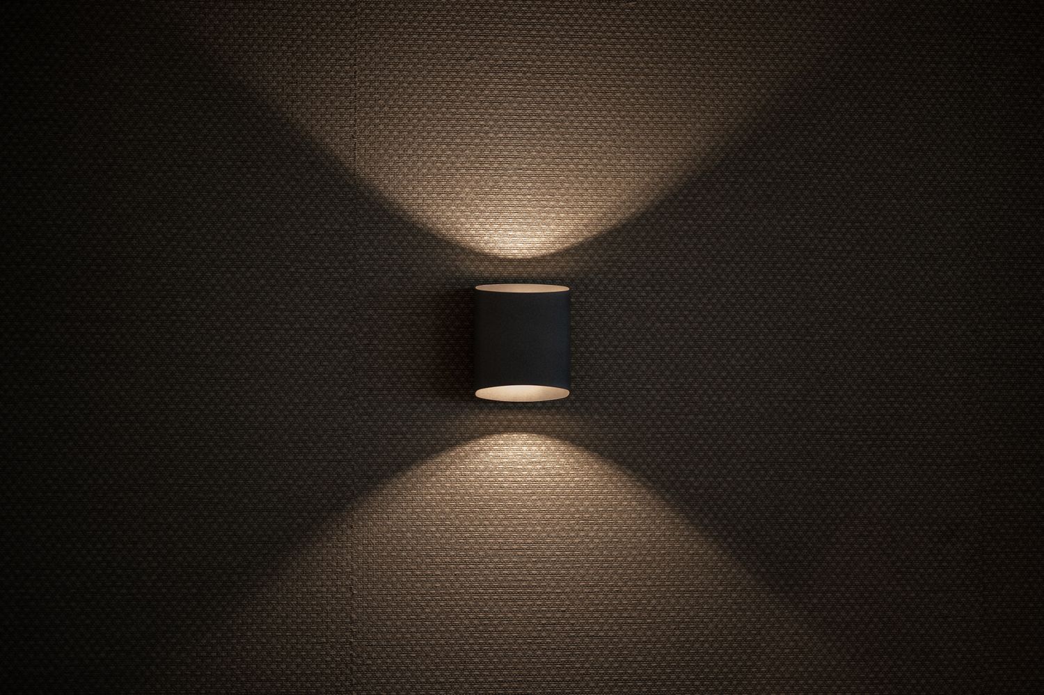 Black wall sconce creating dramatic up and down lighting pattern on textured surface, by Parallel Studios