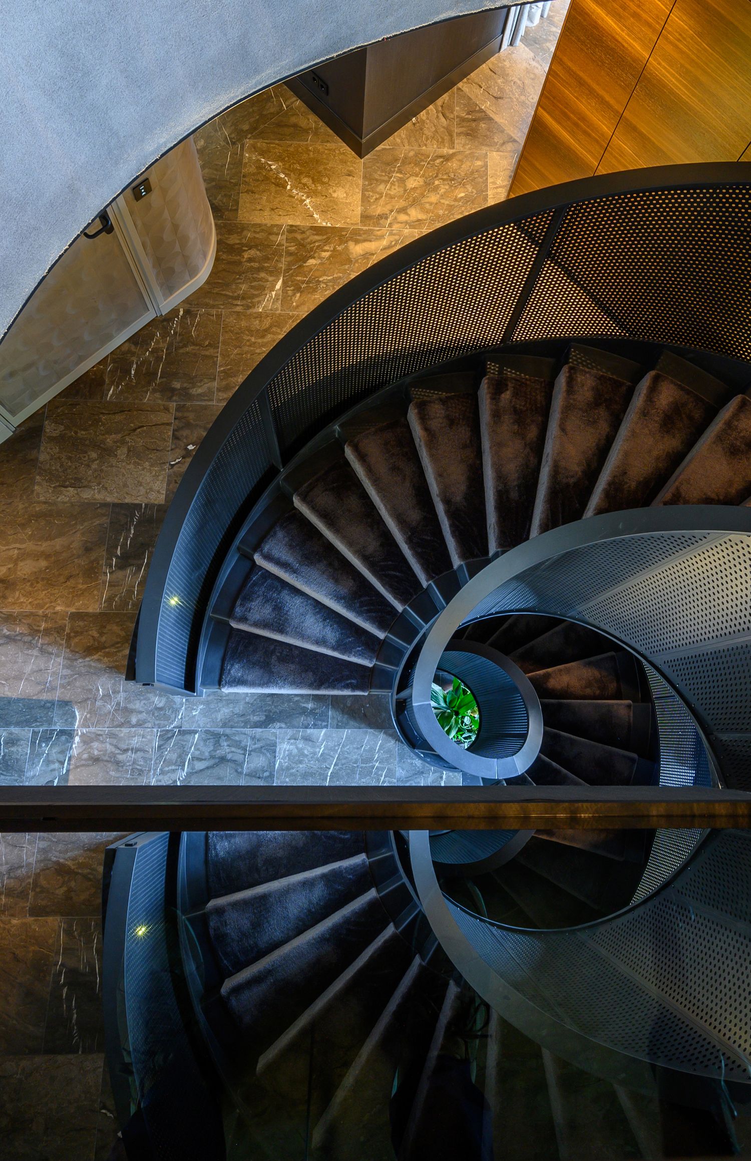 Spiral staircase viewed from above with modern metal and stone design elements.