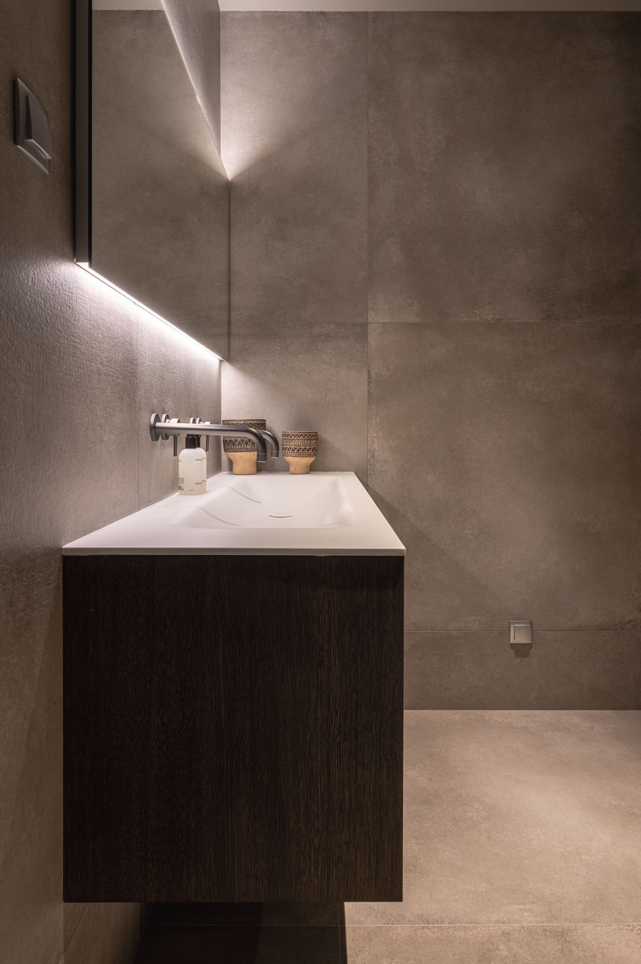 Modern bathroom vanity with sleek lighting and concrete walls creating dramatic shadows.