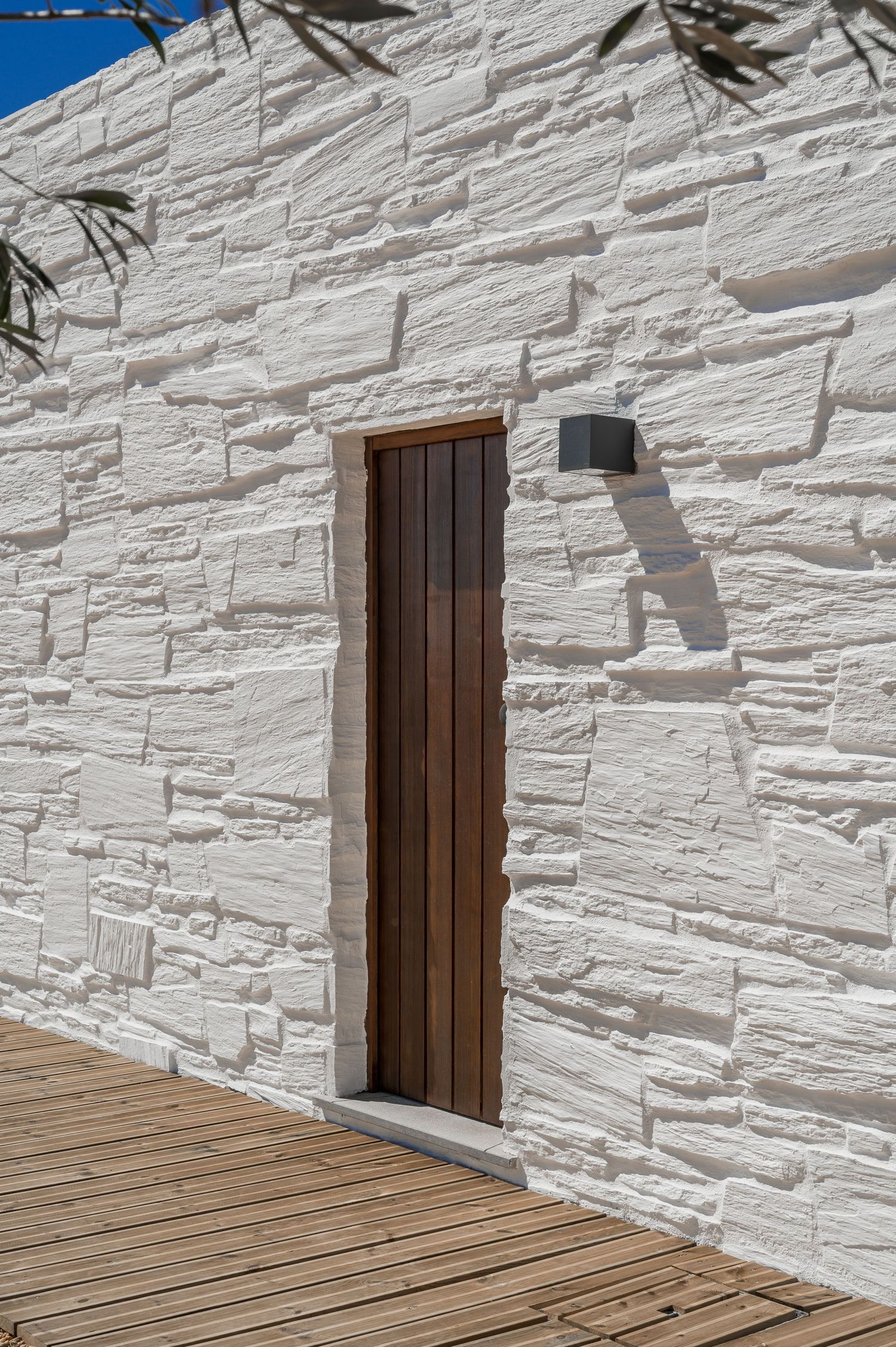 White stone wall with wooden doors and deck creating minimalist architectural detail in the Algarve, by Parallel Studios