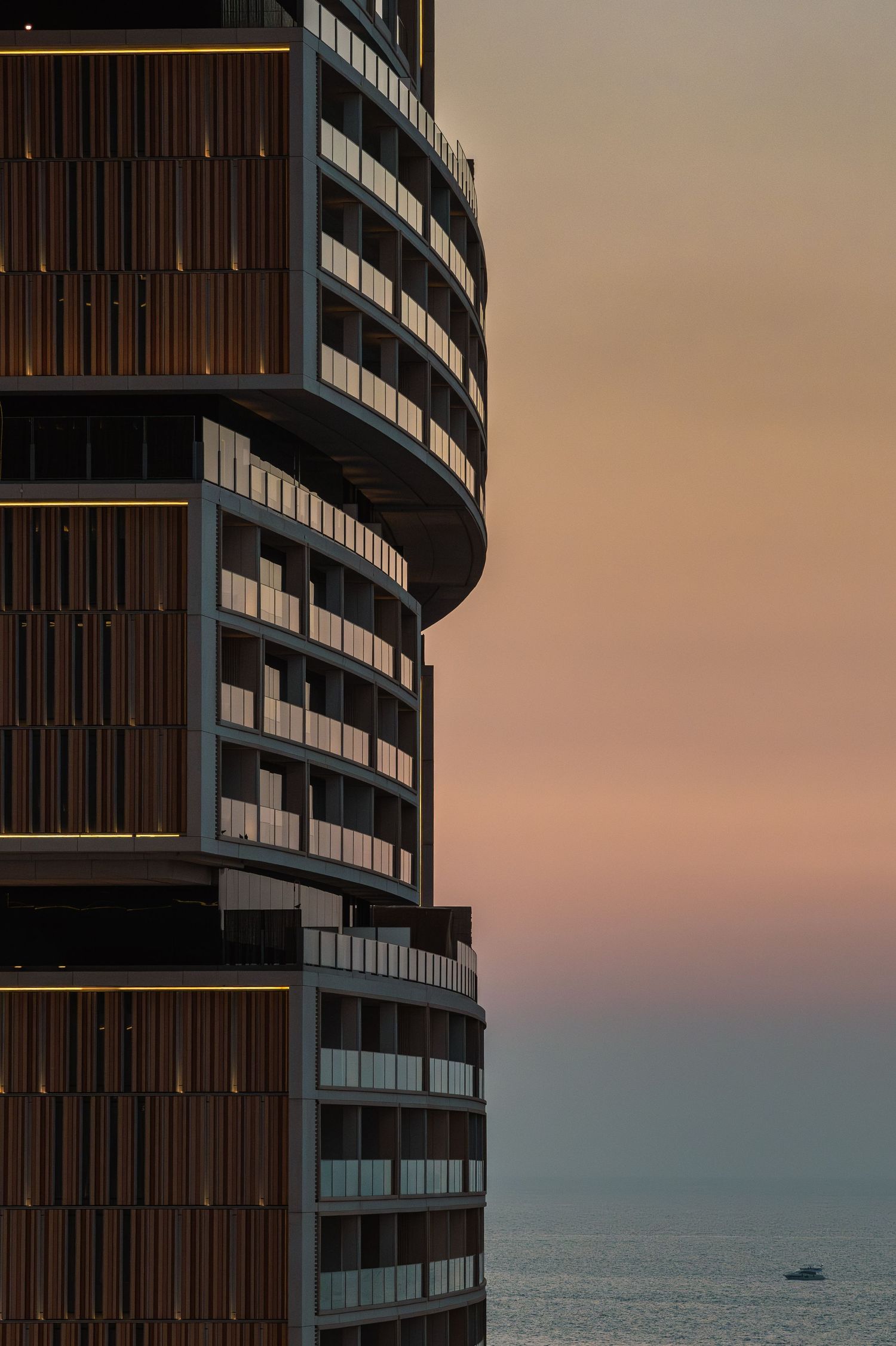 Modern curved apartment building with dark wood panels and glass windows against a sunset sky over the ocean in Dubai by Parallel Studios