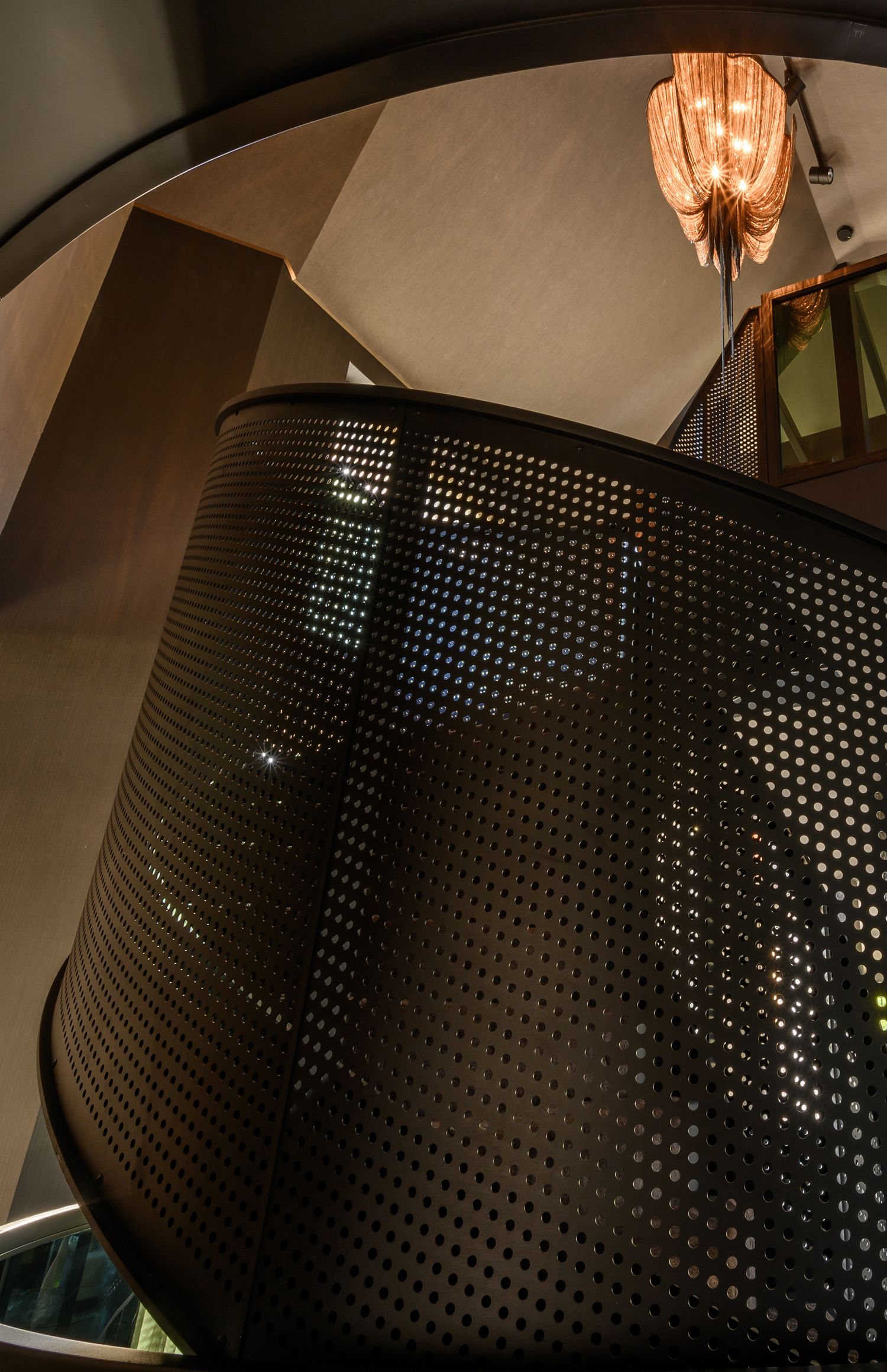 Curved perforated metal wall with dramatic lighting creating geometric shadow patterns.