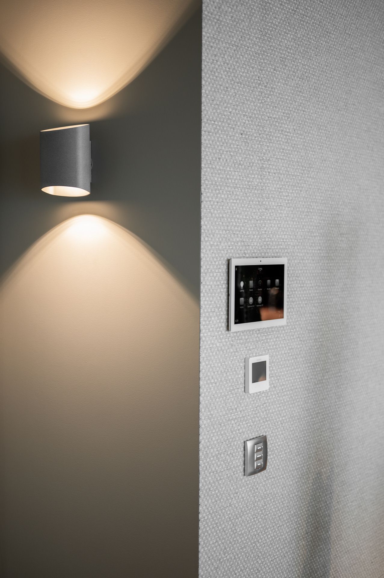 Contemporary wall sconce creating dramatic light patterns on textured grey wall surface.