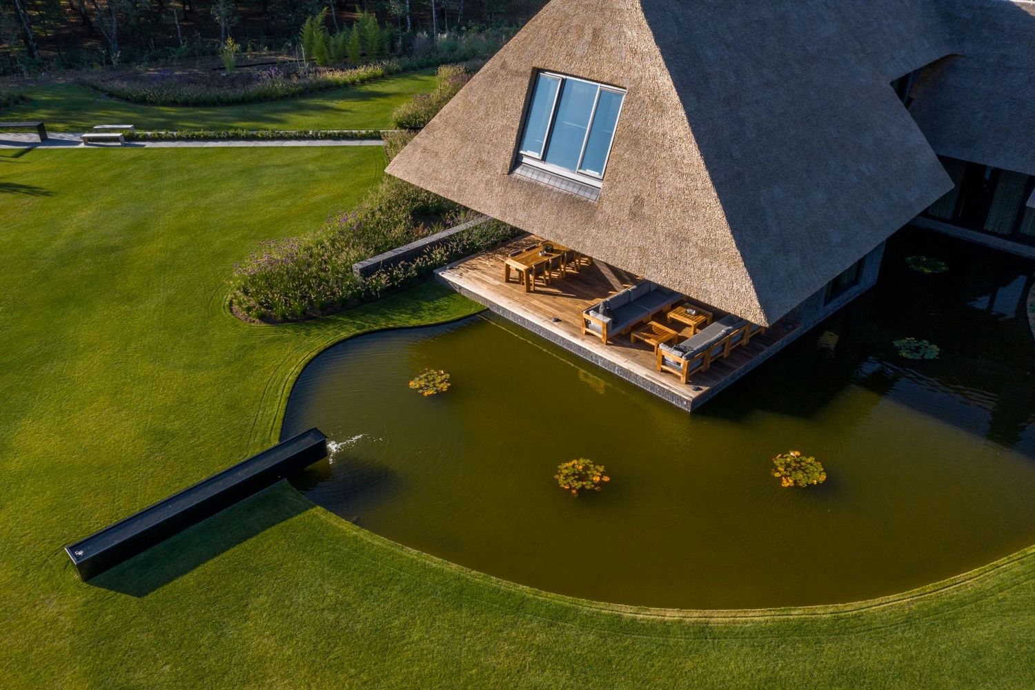 A-frame building with a deck overlooking a serene pond surrounded by manicured lawn, by Parallel Studios