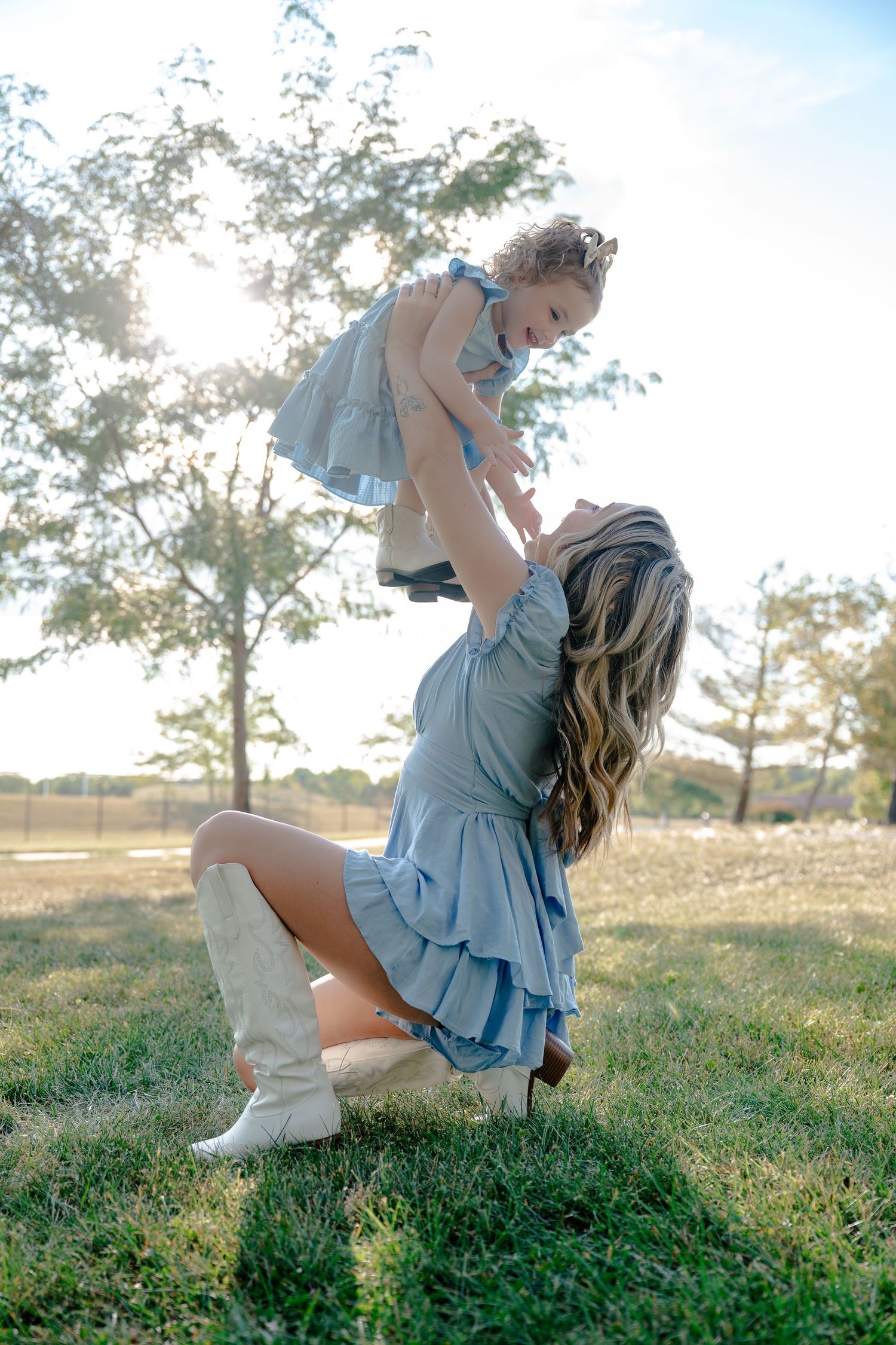 A mother and child play together in a grassy field on a sunny afternoon.