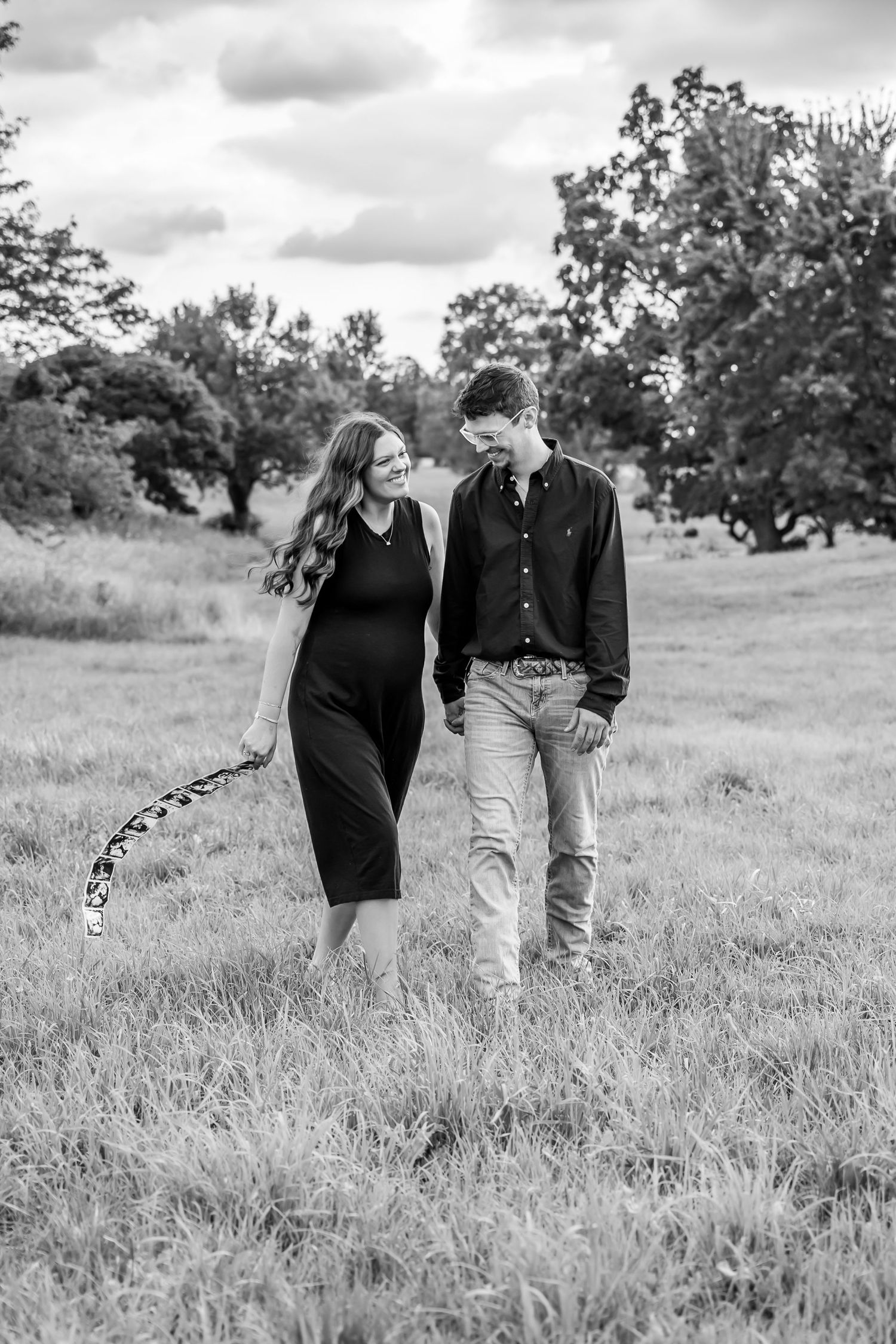 A couple walking together in a grassy field on a cloudy day, captured in black and white photography.