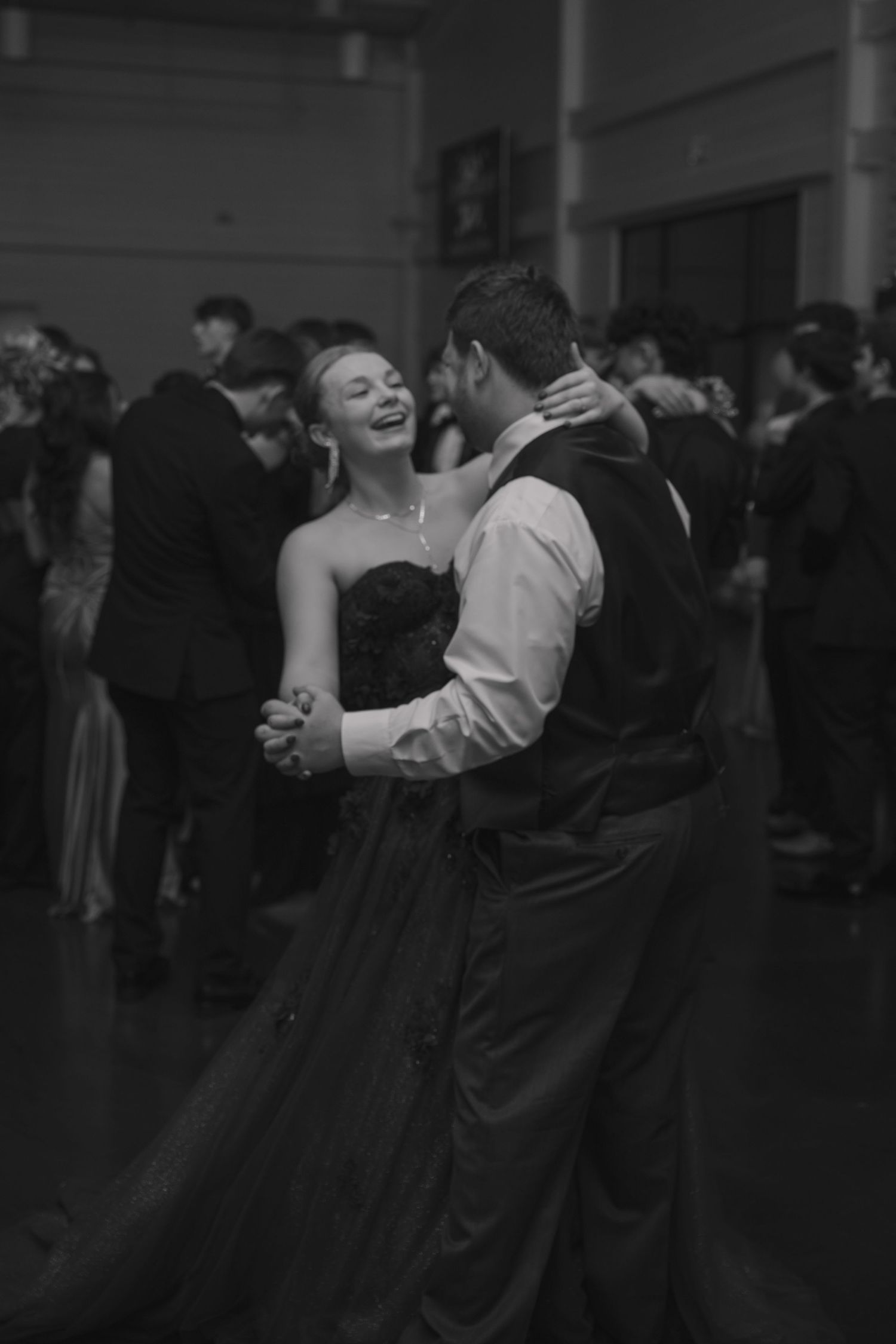 A couple shares a romantic dance moment in formal attire at what appears to be a prom or formal event.