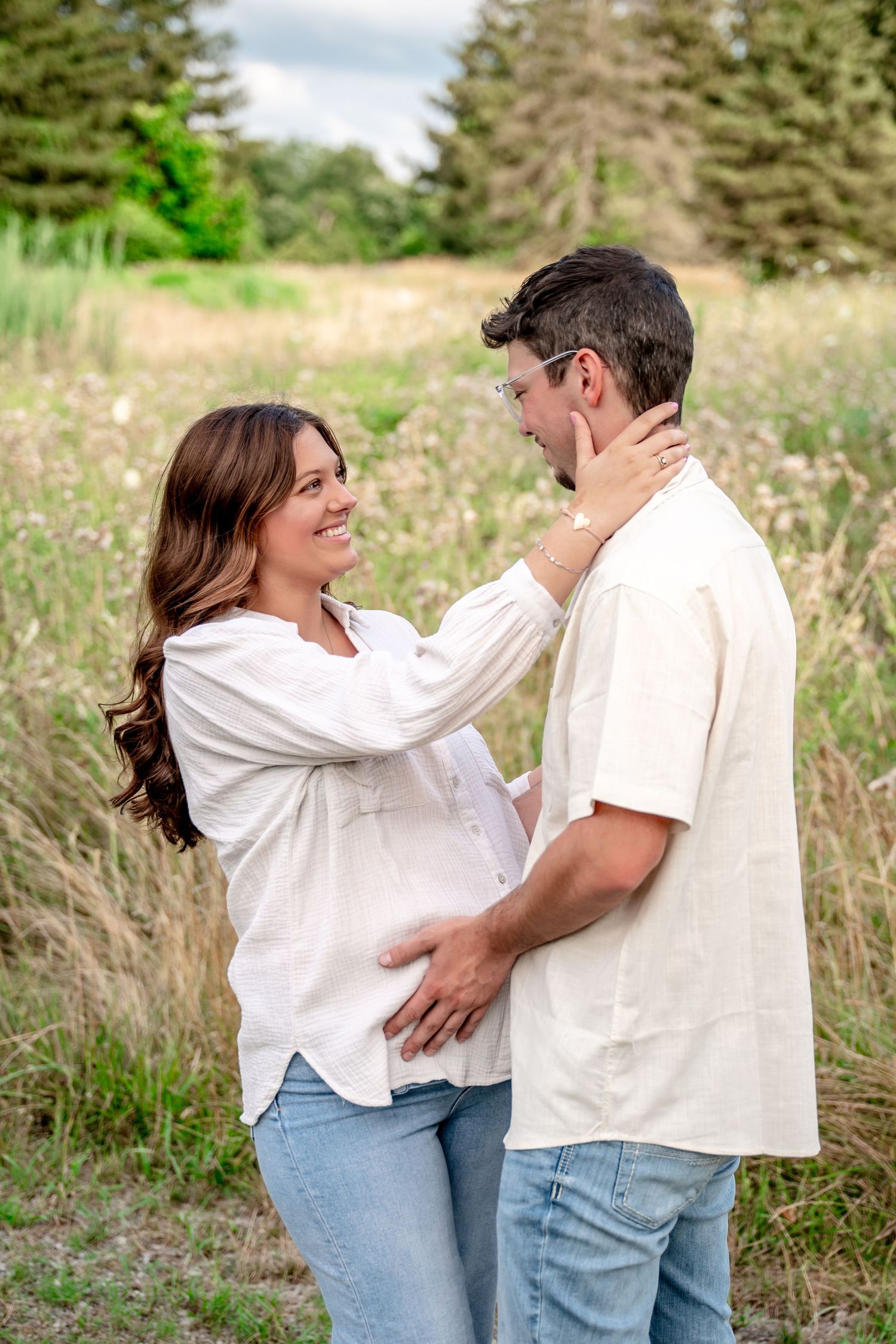 Expectant couple shares tender moment together in a field of wildflowers on a summer day.