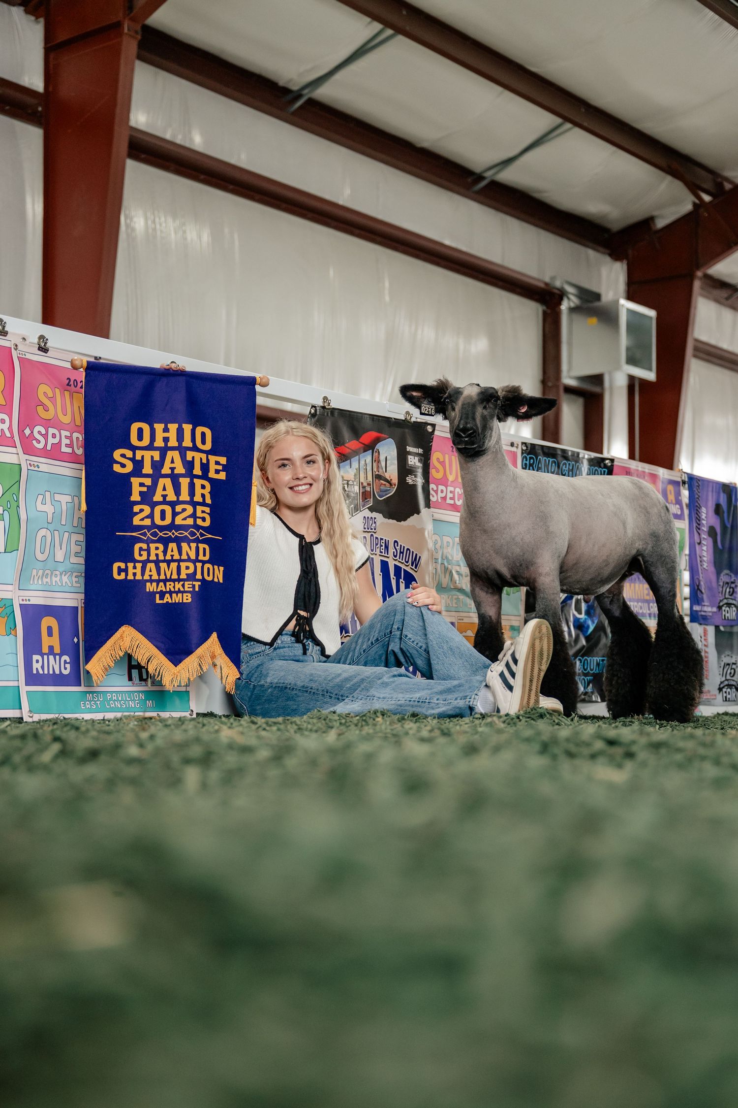 A young exhibitor sits with their prize-winning sheep at the 2023 Ohio State Fair championship showcase.