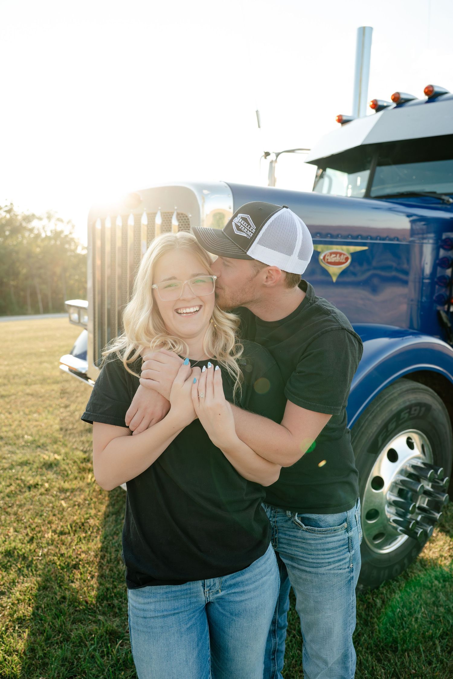 A couple shares a playful moment in front of a vintage blue truck during a golden sunset photoshoot.