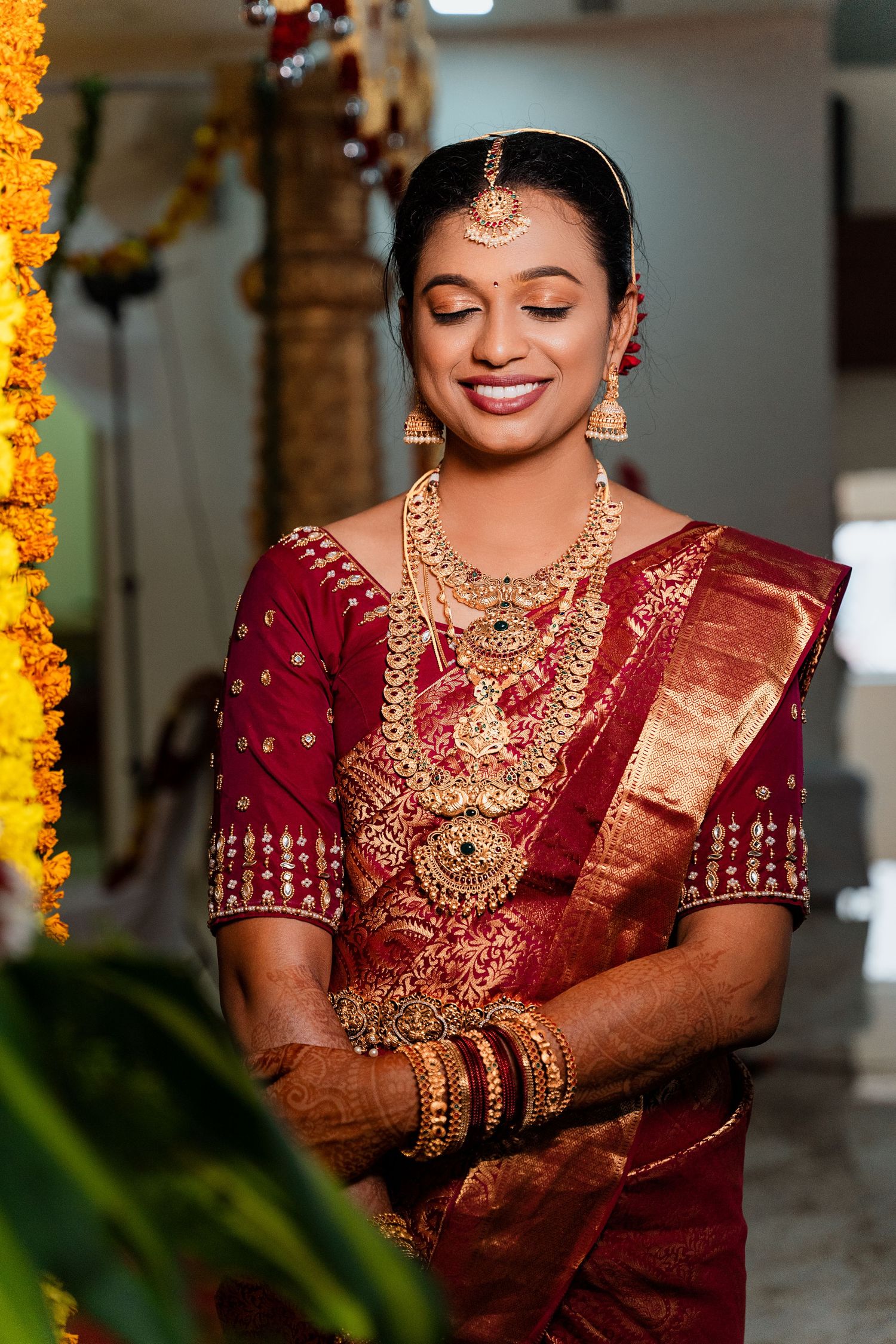 Traditional South Indian bride in red silk saree with ornate gold jewelry and henna designs.