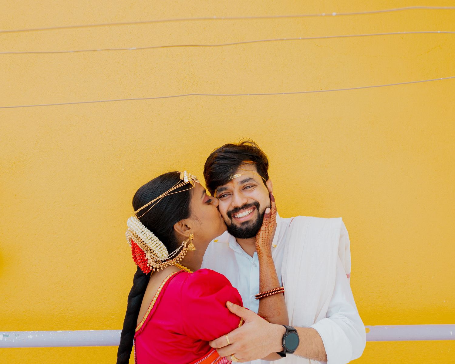 A couple shares a joyful moment against a bright yellow wall background.