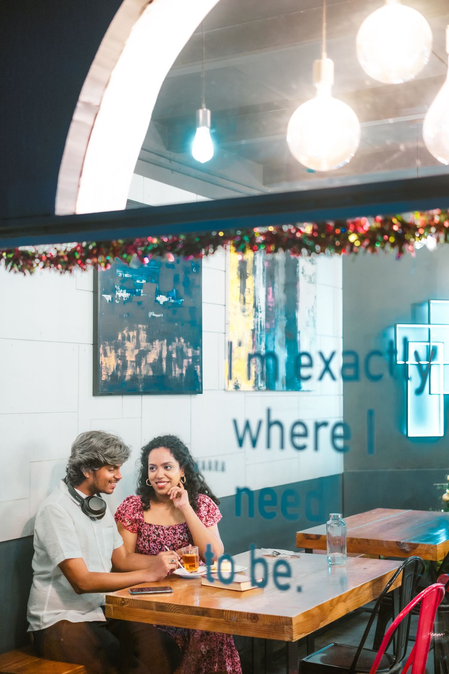 A couple shares a romantic moment at a cozy restaurant with hanging lights and floral decor.