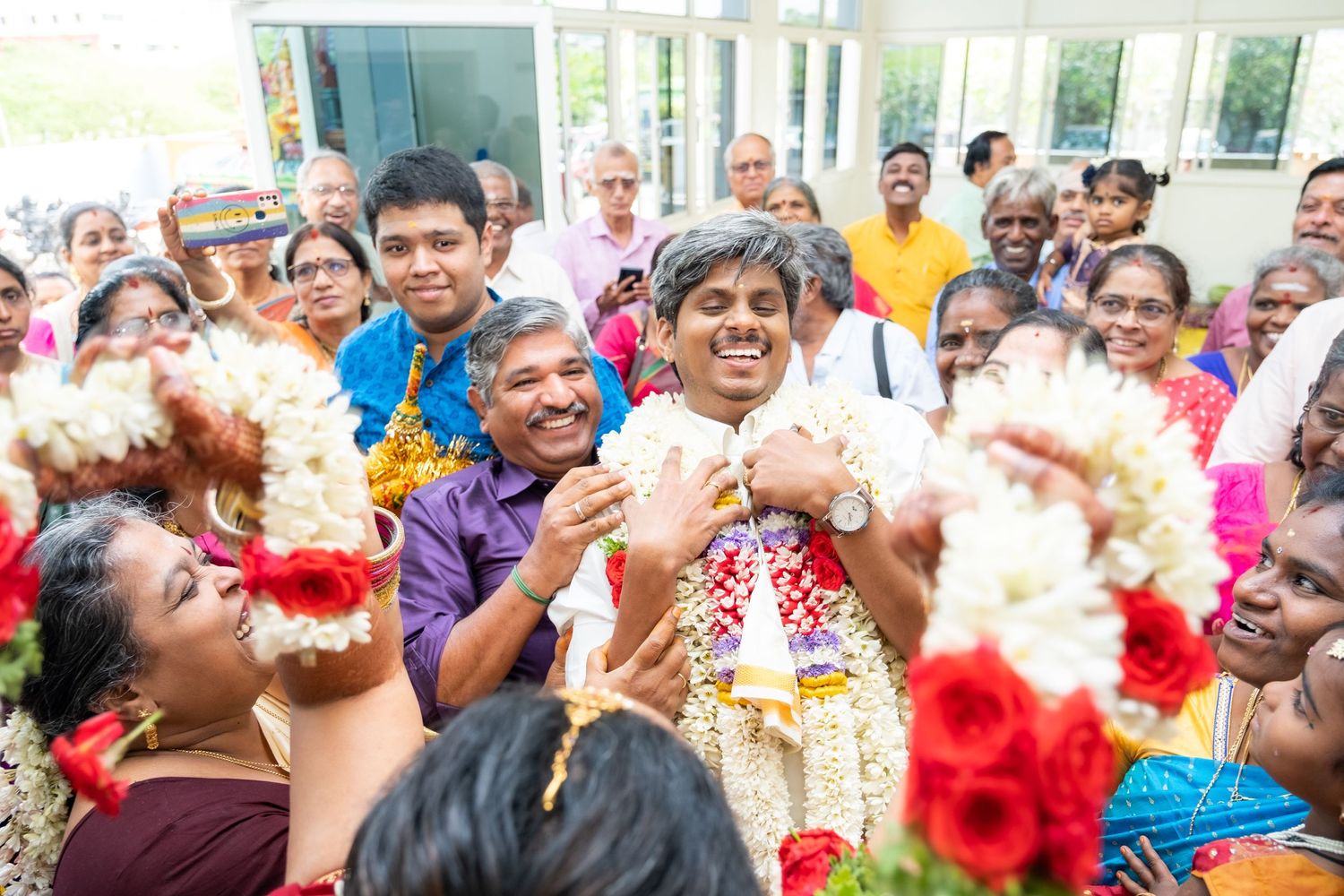 A joyous crowd celebrates with vibrant red and white floral garlands during a traditional Indian ceremony.