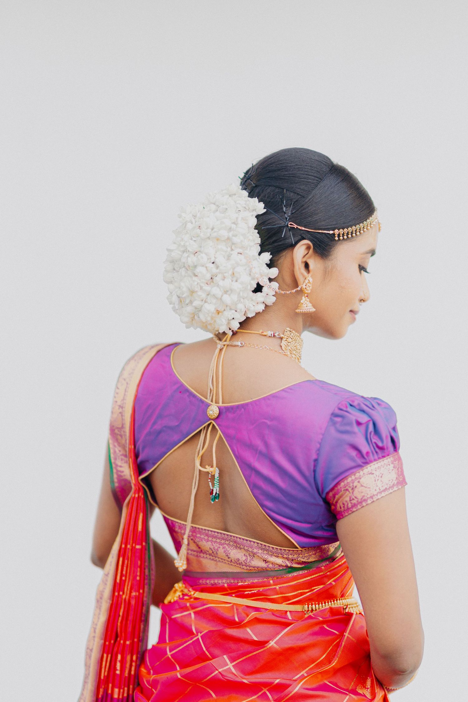 Elegant bridal attire featuring a purple blouse and red silk saree adorned with traditional white floral hair ornaments.