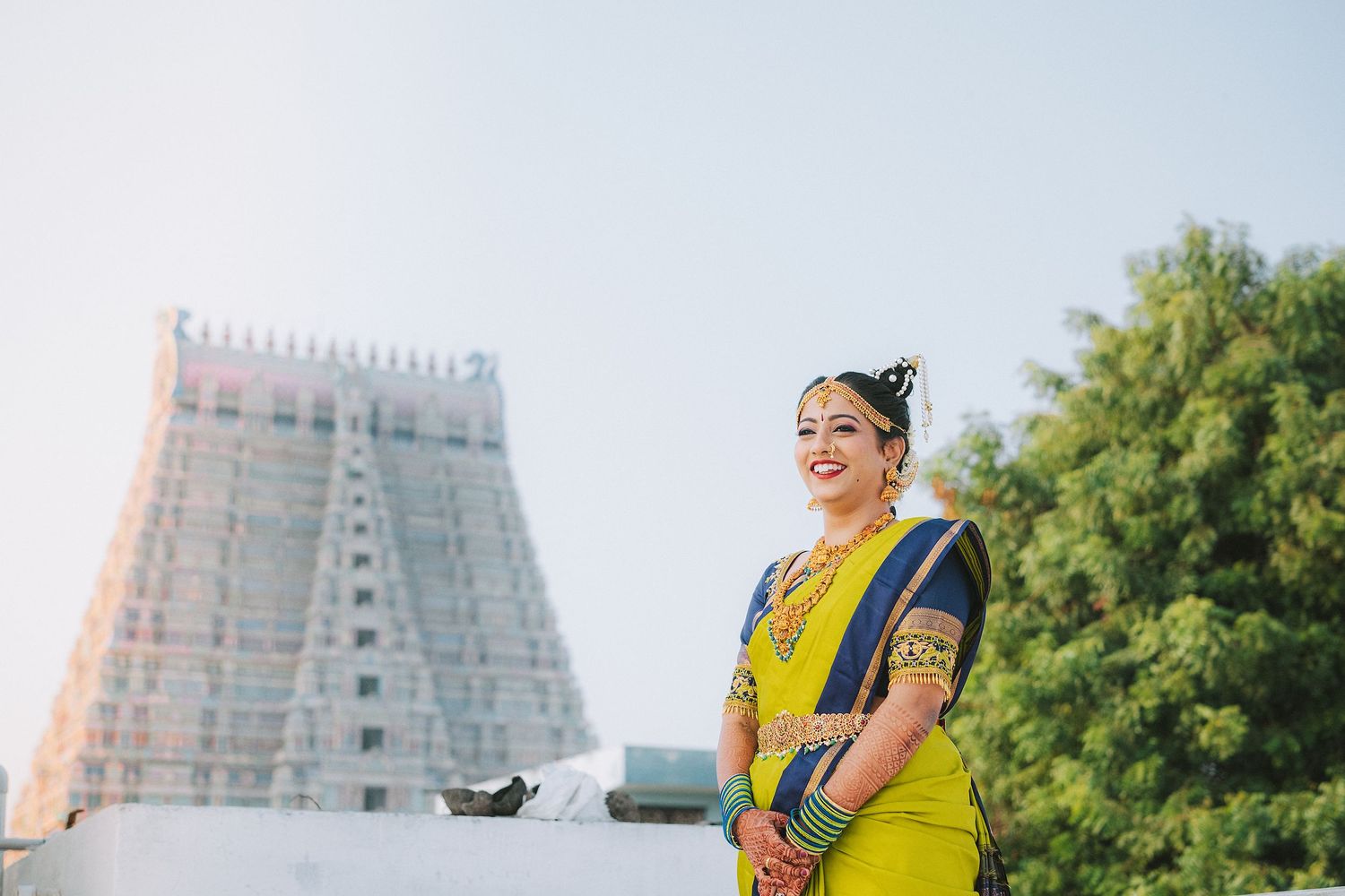Bright yellow traditional outfit contrasts beautifully against white temple architecture and blue sky.