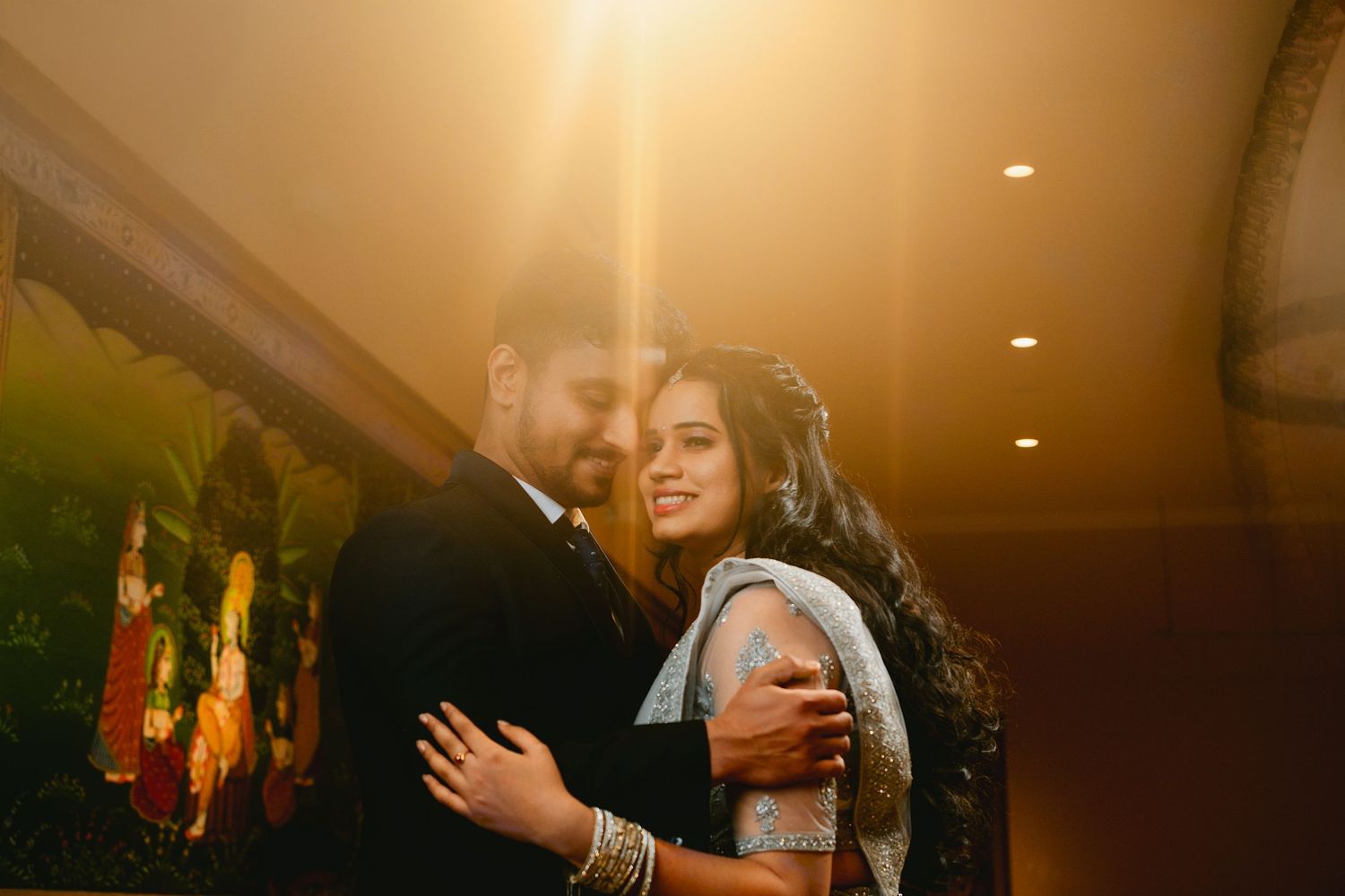 Couple in formal attire share romantic moment under warm lighting at reception.