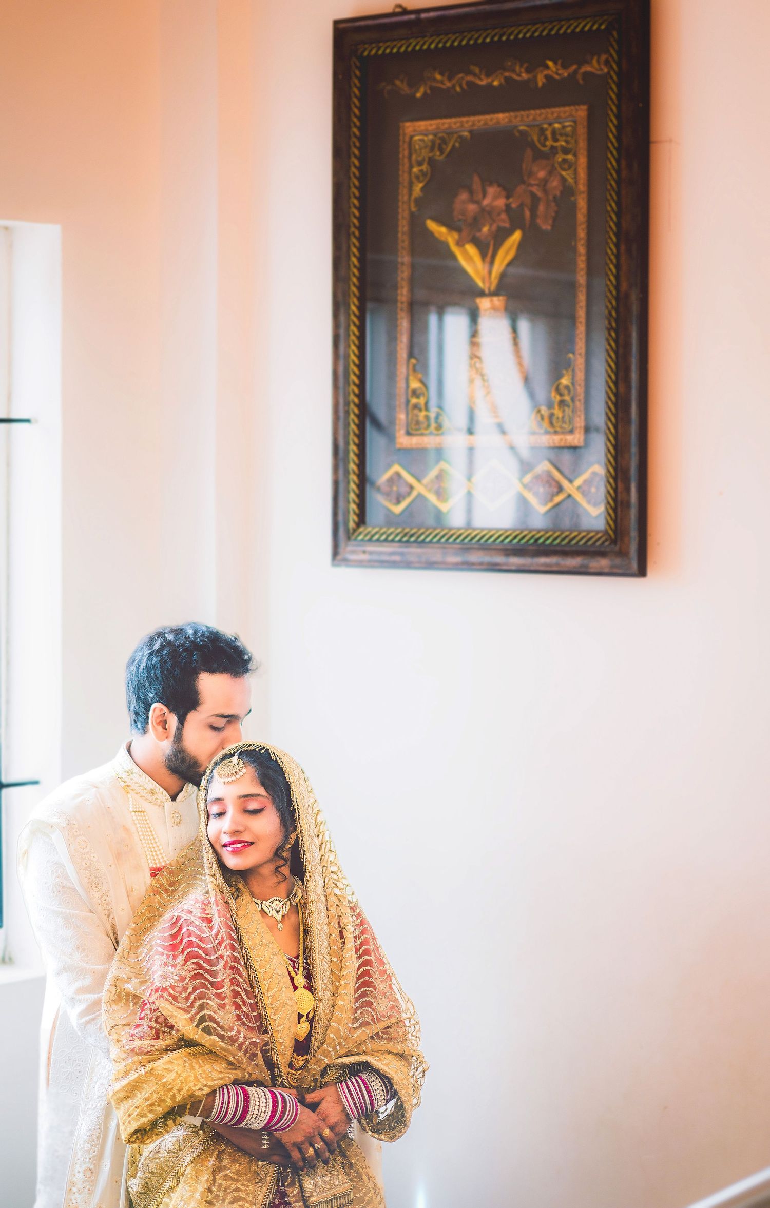 Traditional Indian wedding attire shown in intimate indoor portrait with decorative wall art.