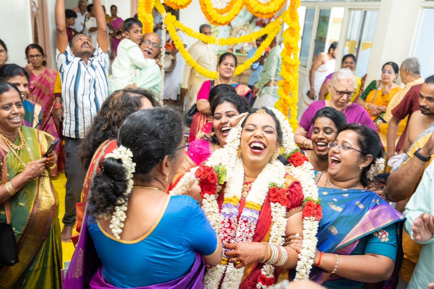 Guests laugh and celebrate during a festive Indian wedding ceremony adorned with yellow and orange decorations.