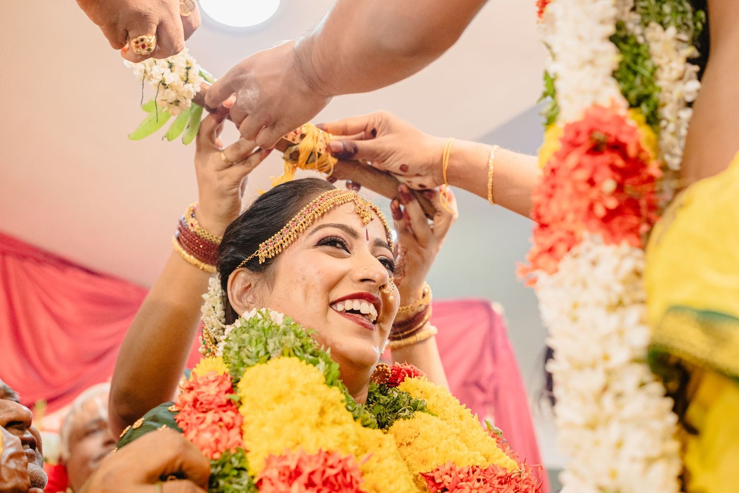Traditional Indian wedding ceremony showing turmeric application ritual with colorful floral decorations.