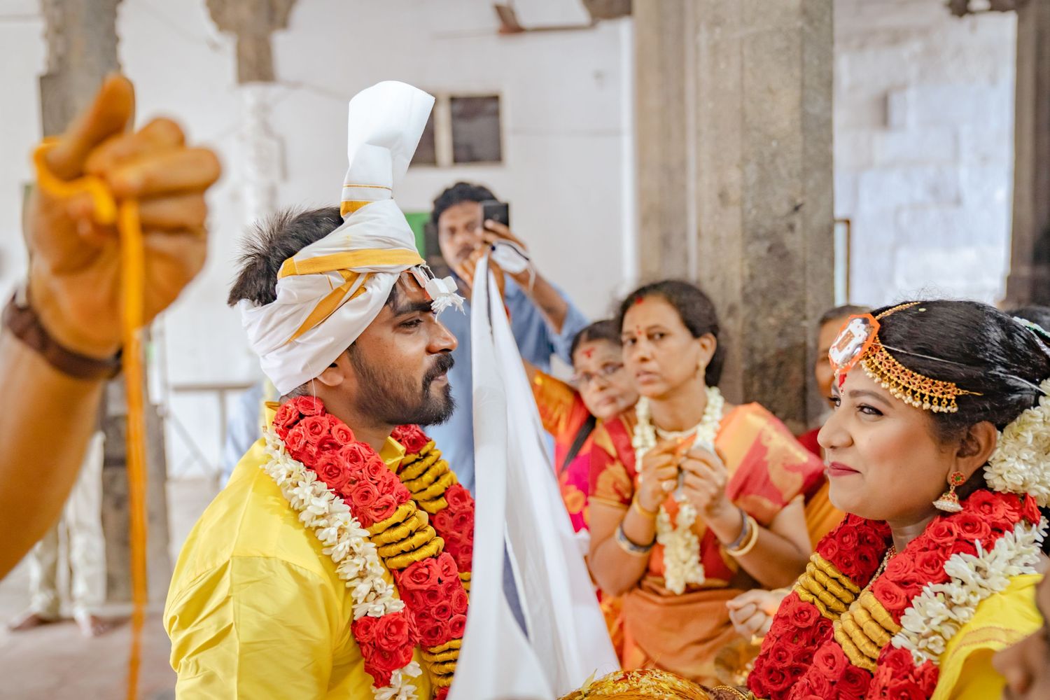 Celebrants in yellow and orange attire participating in a traditional ceremony with floral garlands.