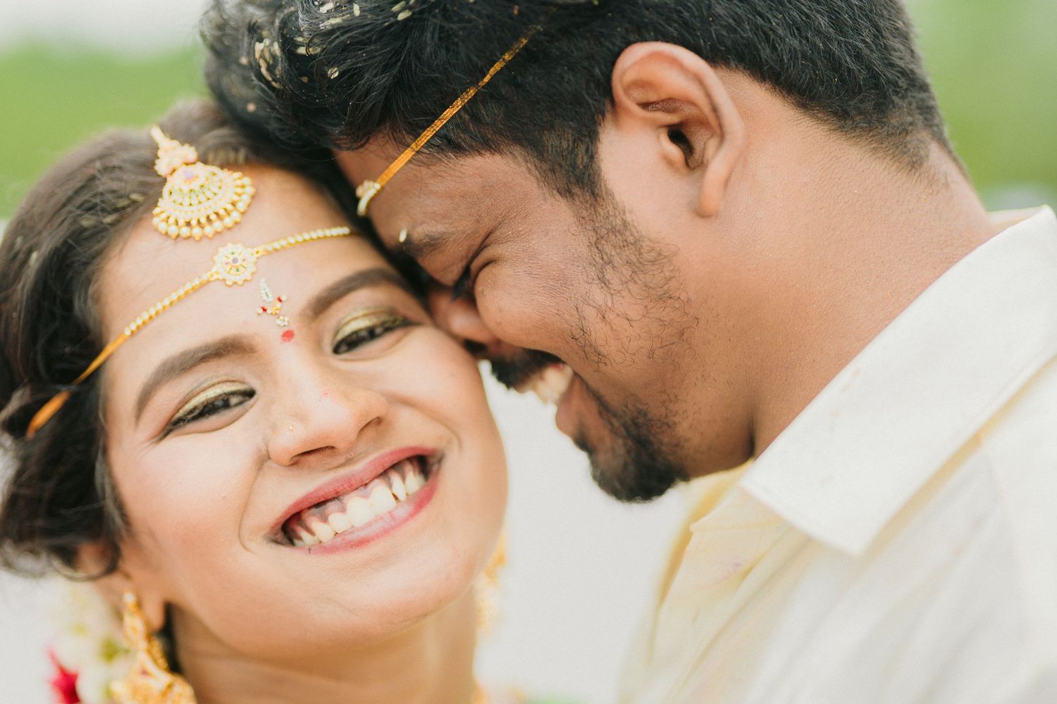 Close-up portrait of couple in traditional Indian wedding attire sharing joyful moment outdoors.