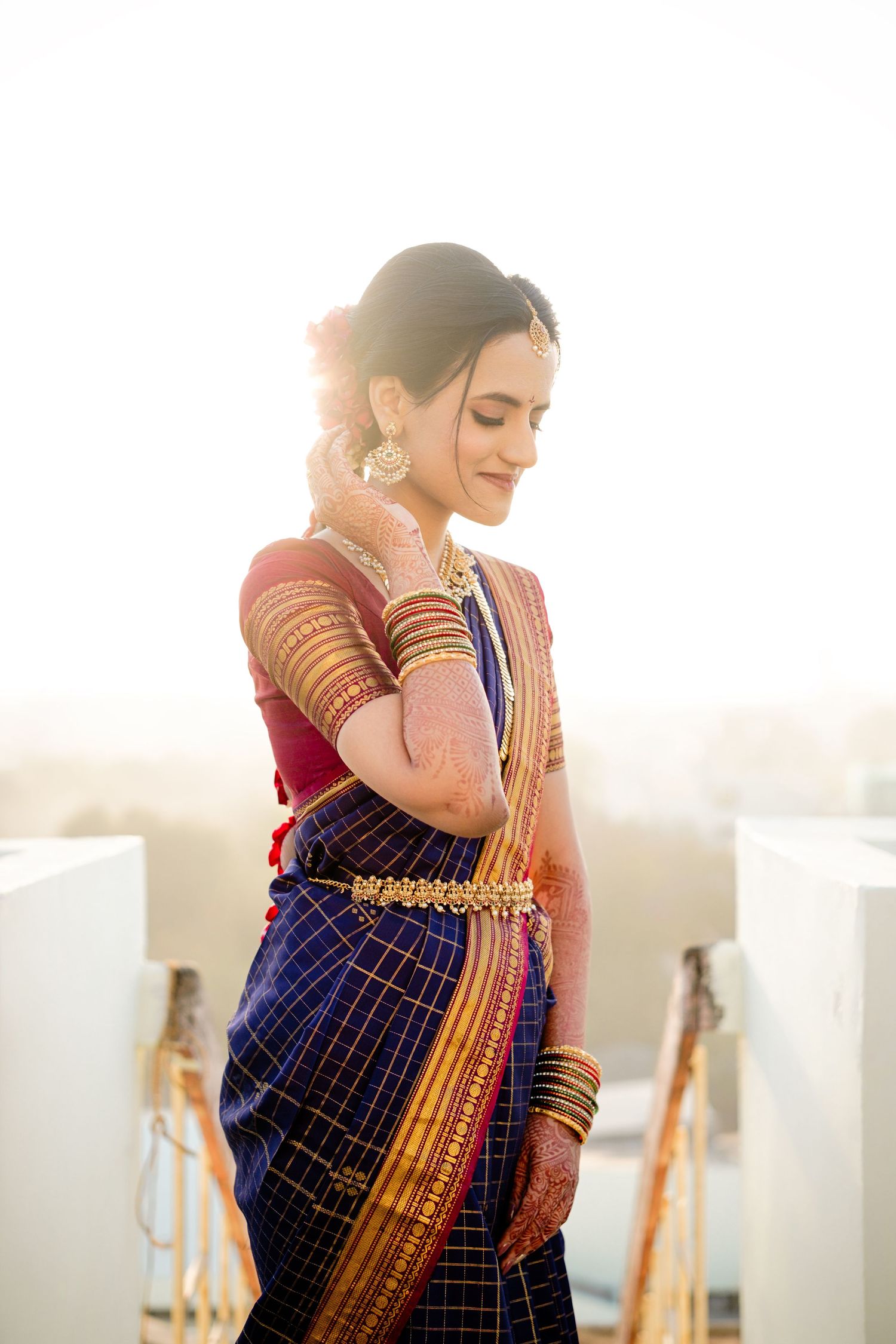 A woman in traditional South Indian silk saree and jewelry poses gracefully in golden sunlight against a bright background.