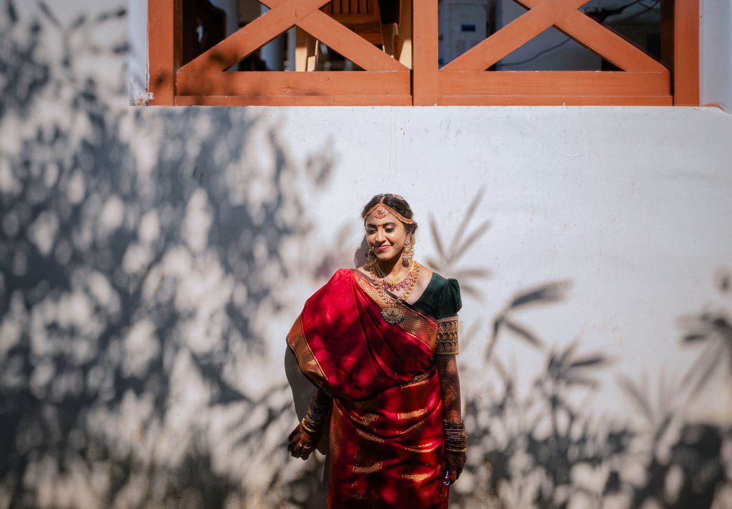 Figure in vibrant red traditional dress posing near architectural window with shadows.