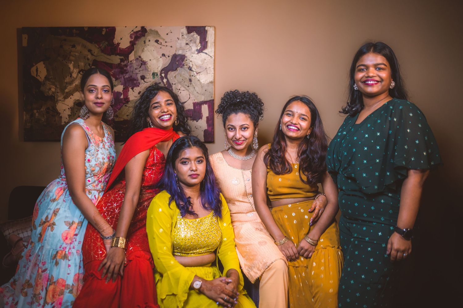 Group photo featuring women in colorful traditional Indian dresses against abstract wall art.
