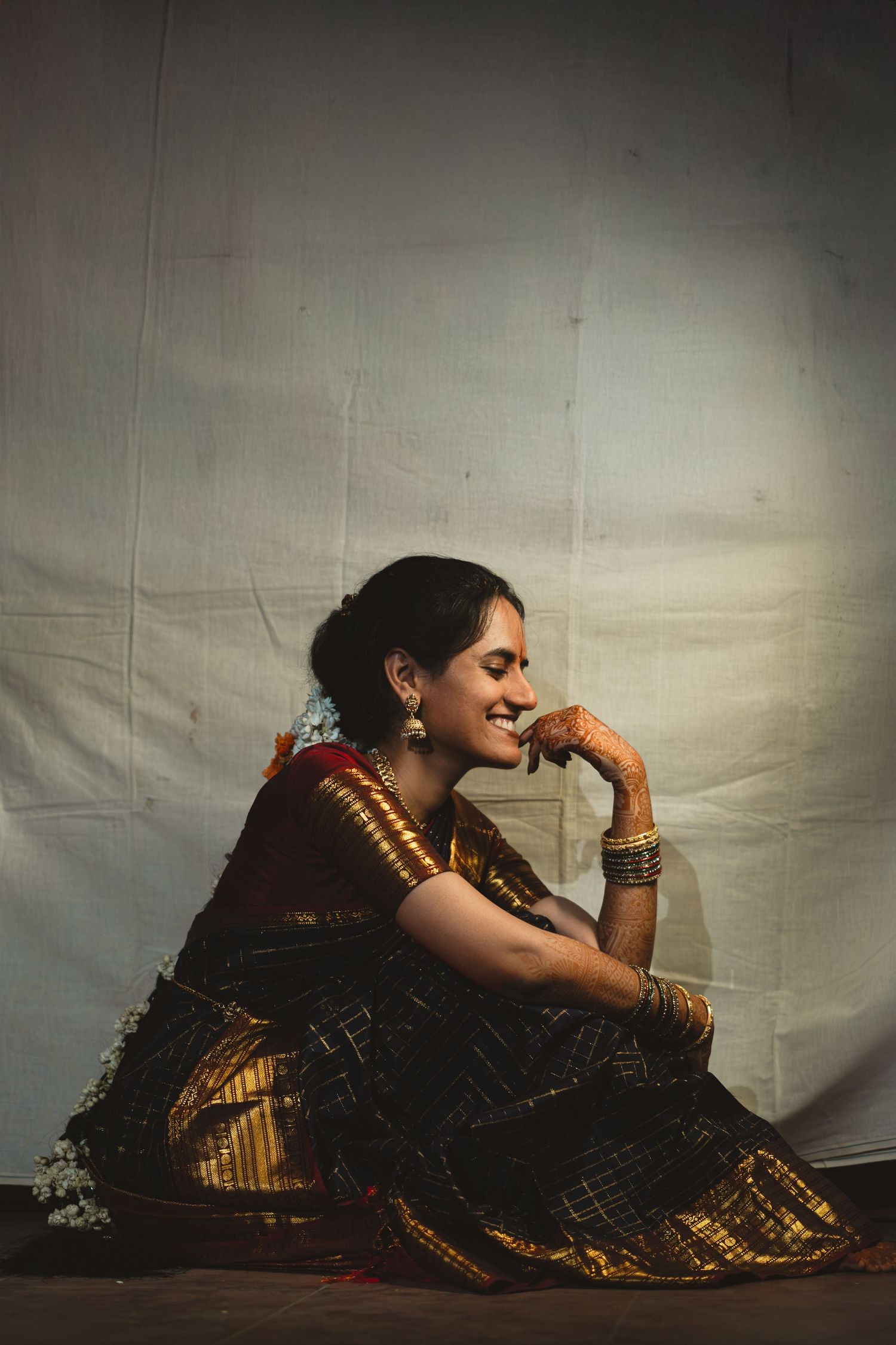 A figure in a traditional Indian sari with gold accents reclines gracefully against a dark backdrop in a photo series.
