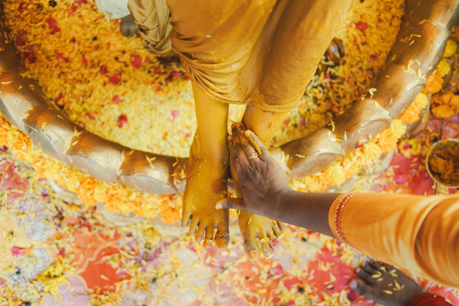 Colorful turmeric powder being applied during a traditional Haldi ceremony with hands and yellow fabric.