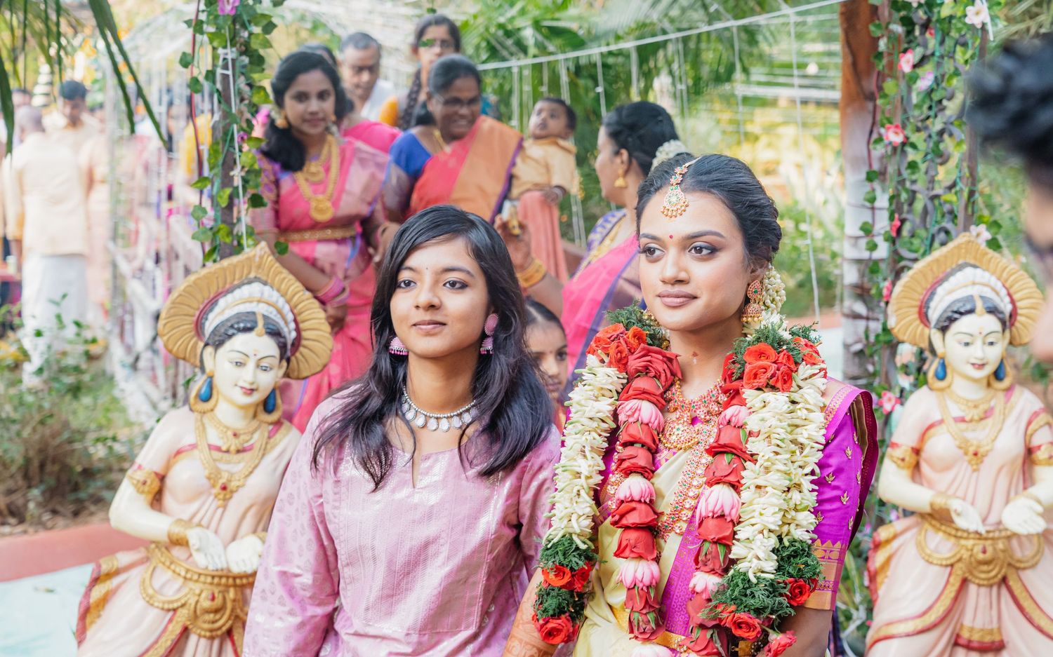 Outdoor garden ceremony with decorative statues and ladies in traditional attire.