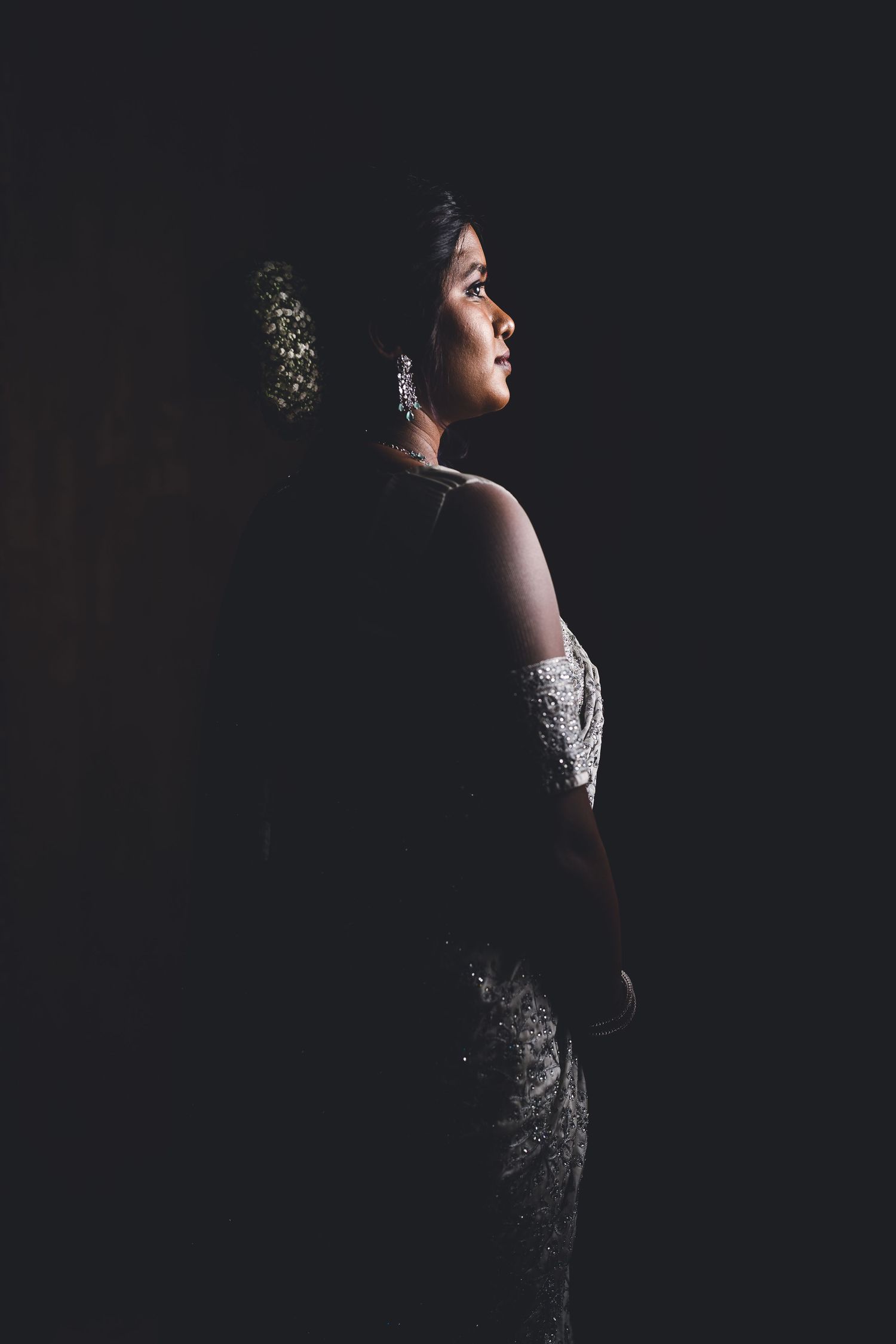 Dramatic side-lit portrait of a figure in an elegant white dress against a dark background.