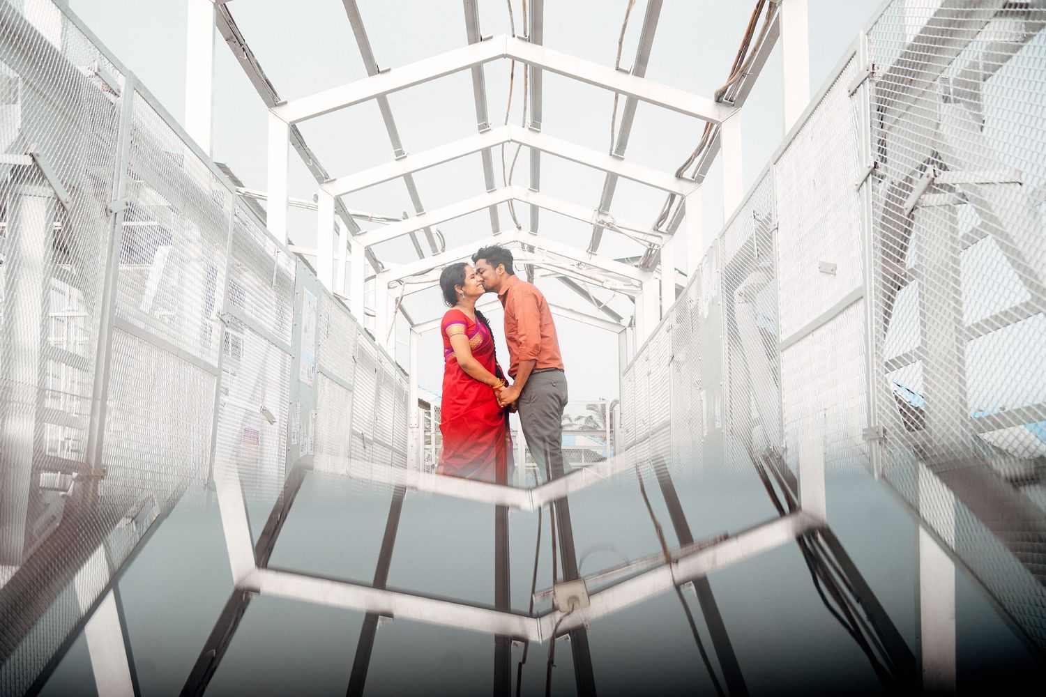 Modern couple in stylish attire pose in futuristic white corridor setting.