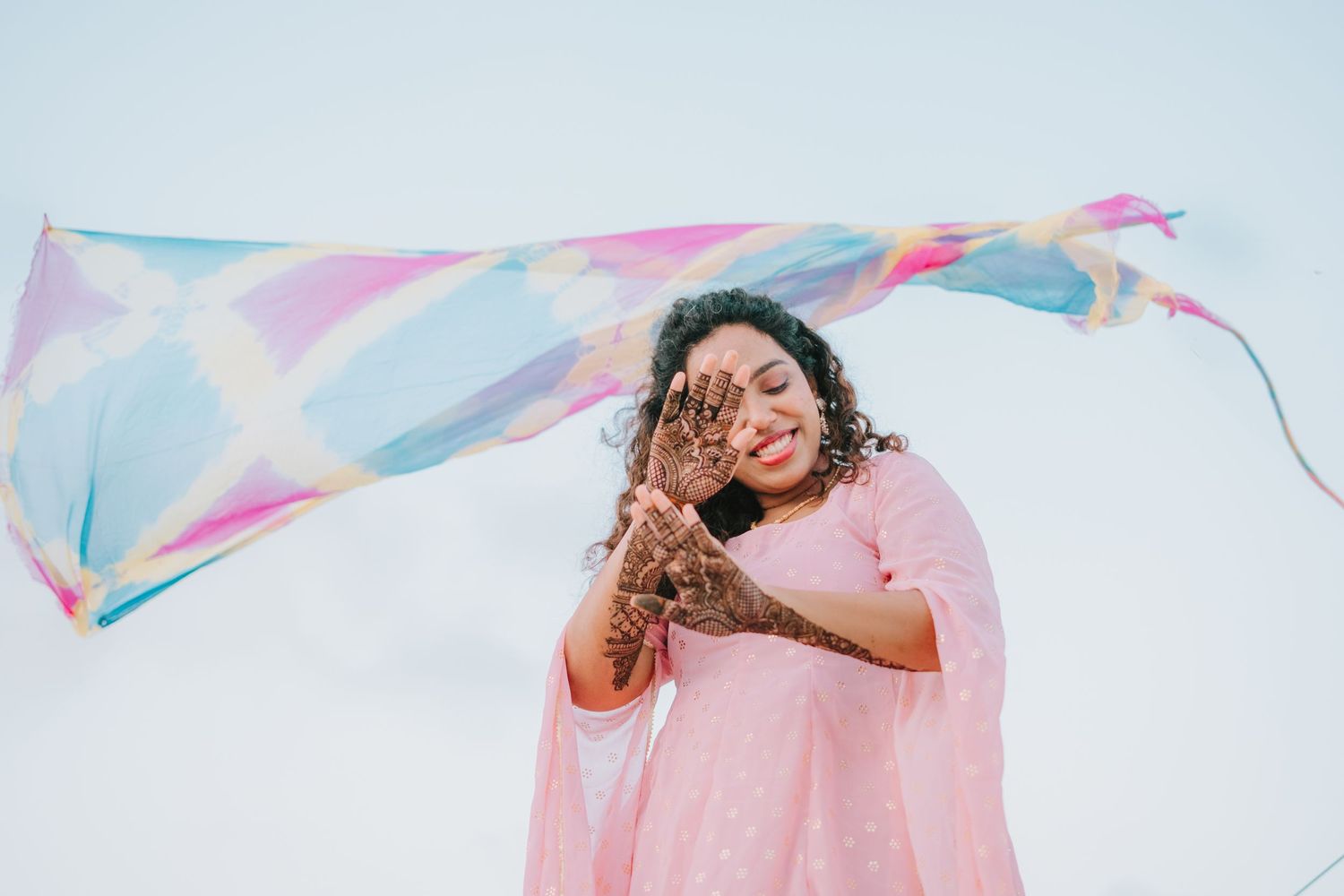 A person in a pink dress laughs joyfully while a colorful streamer flows behind them in the breeze against a blue sky.